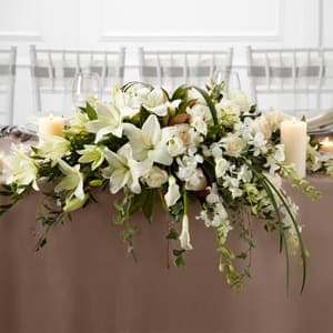 White Linen Arrangement - The White Linen Arrangement speaks to the true nature of wedding elegance. White Dendrobium Orchids Asiatic Lilies mini calla lilies and roses are accented with an assortment of lush greens and arranged to add to the décor of the wedding party's table with its sweet sophistication.