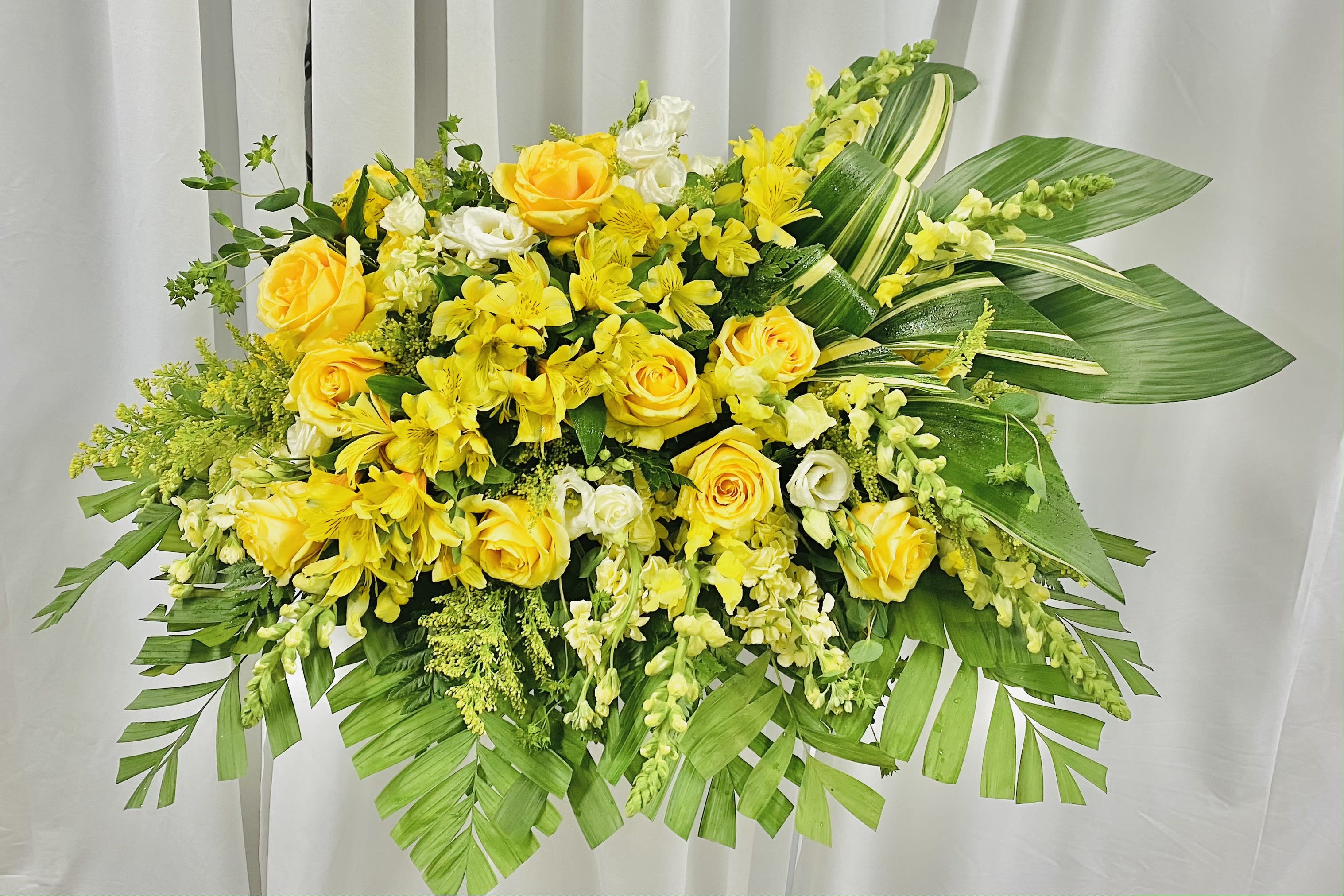 Twist of Serenity - A striking twist on a traditional casket spray.  This design features a line of alstromeria from one end of the arrangement leading to a strong display of variated leaves.  Roses, lisianthus, snapdragon, belpernum, and more accent the display.
