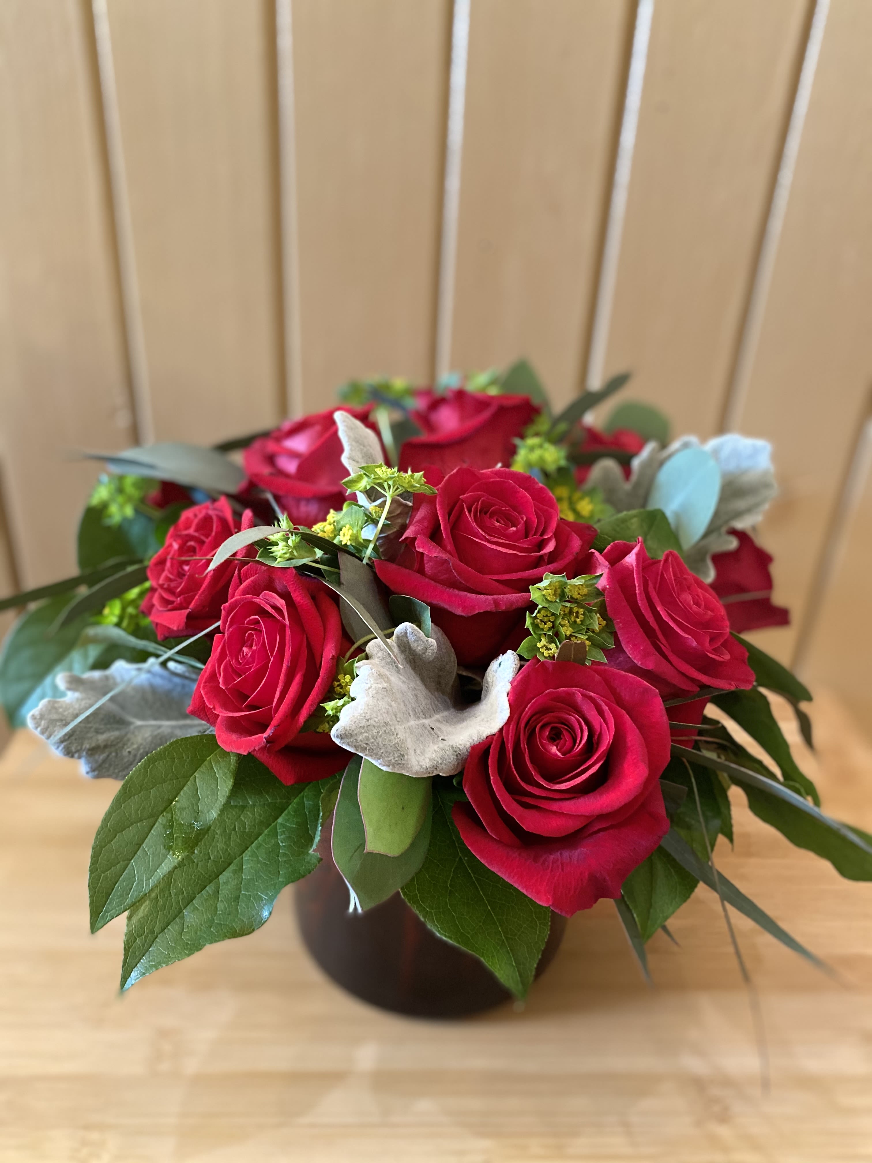 Modern Love - A different take on a dozen roses.  Presented in a cropped red cylinder vase, and accented with eucalyptus and silver foliage.  Perfection in simplicity.   (Upgraded pricing will include more roses and curly willow accents.)