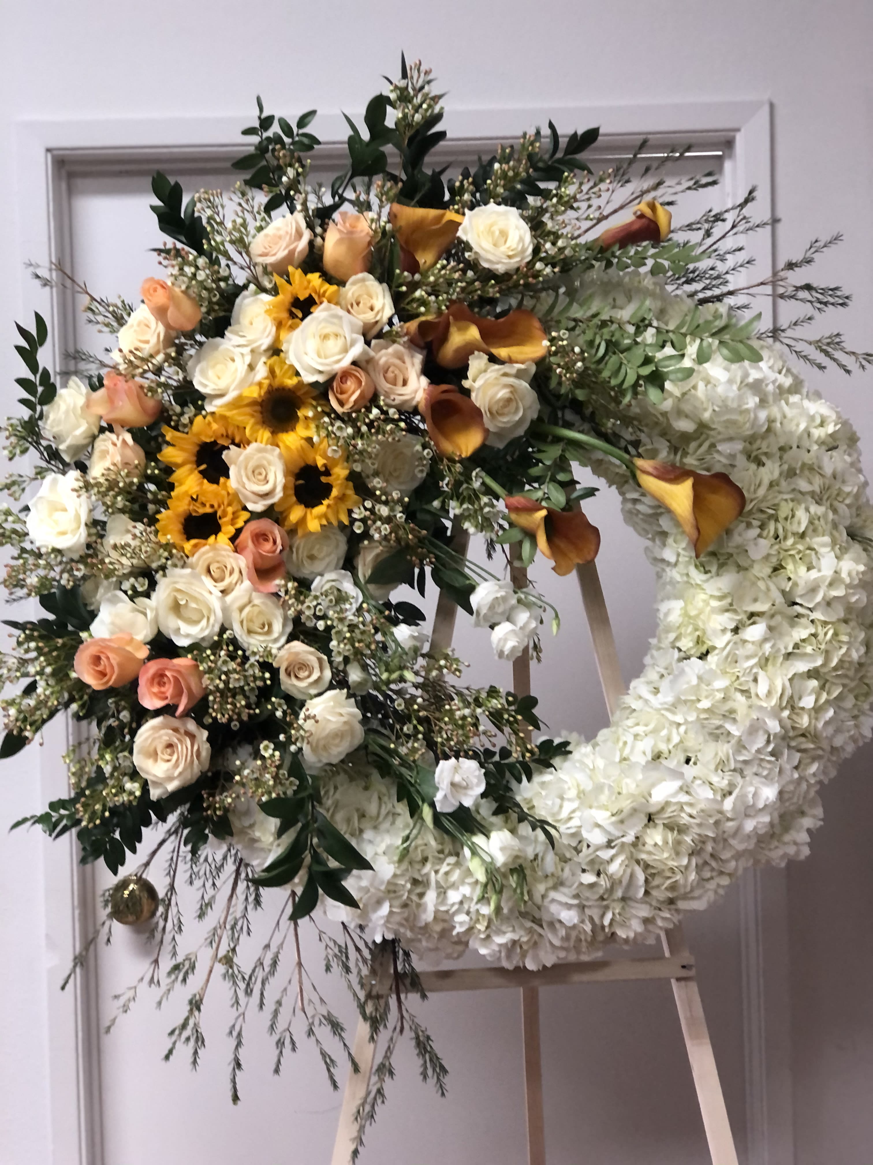 Funeral 3 - White wreath with orange and yellow flowers cascading on one side.