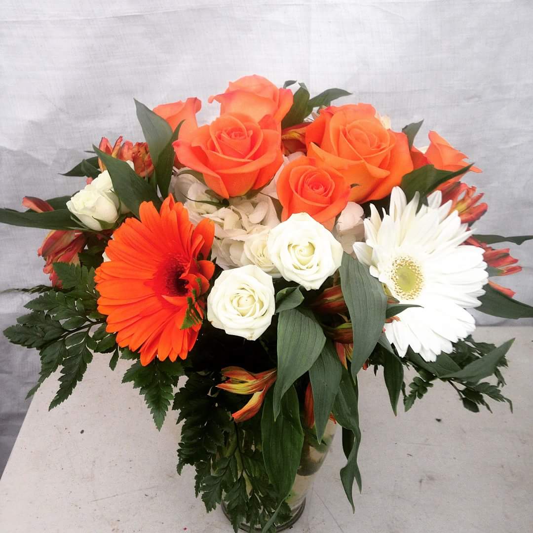 Heaven Scent - This arrangement includes, orange roses, white spray roses, white hydrangea, Gerber Daisies and  alstroemeria, in a clear glass vase.
