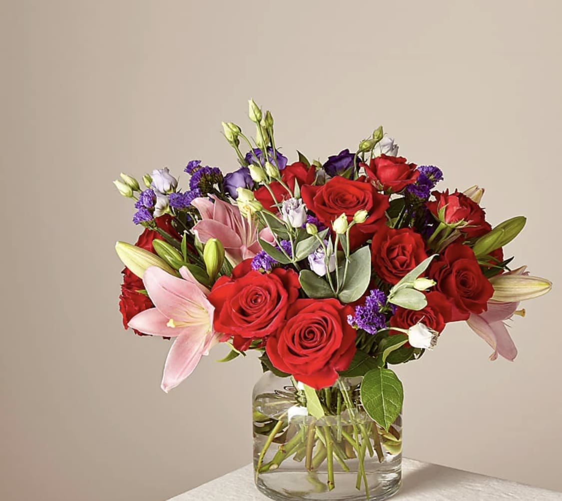 Truly Stunning Bouquet - Share a smile with your loved ones through a bouquet filled with stunning beauty and heartfelt joy. Comprised of vivid red roses, purple double lisianthus, pink lilies and red spray roses within a clear glass vase, vibrant color bursts from every bloom. Make their day brighter with a gift that is Truly Stunning!