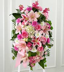 Gently In To The Ever After - Bright, fresh, beautiful and just right for an elegant expression of heartfelt sorrow and devastating loss. This classic standing arrangement is constructed by a  artisan florist of hand-selected pink blossoms ranging from pale pastels to deep blushing pink. It includes roses, carnations, stock, cushion pompons, Asiatic and Stargazer lilies and hydrangea beautifully set among a field of lush contrasting greens like aspidistra and ivy vines. It comes with a wooden easel for flexible display options and makes an impressive memorable tribute at a wake, funeral or graveside service.