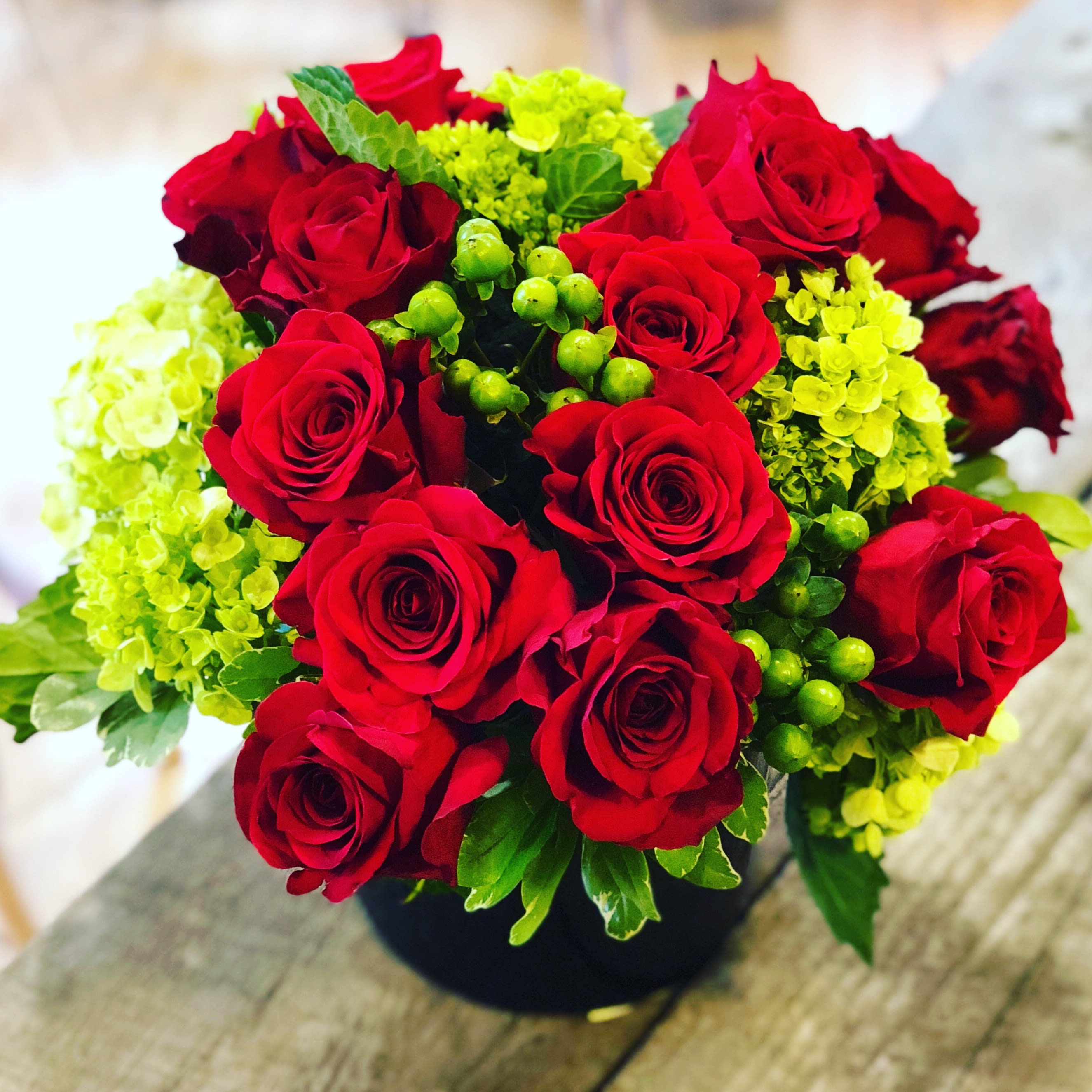 Standout Reds - This arrangement includes a plethora of beautiful freedom red roses sitting atop a bed of bright green hydrangea.  Designed in a contrasting, black vase to really make the blooms pop.