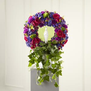 The Faith &amp; Understanding Wreath - This variation on the traditional sympathy wreath includes brilliant jewel-toned blossoms surrounding a figure of the Blessed Virgin and a cascade of ivy that poignantly that reflects your heartfelt tears. This impressive wreath handcrafted in a white ceramic planter by a local florist of hot pink spray roses, purple statice, hydrangeas and magenta button pompons encircles the keepsake ceramic statue of Mary. It makes a beautiful tribute to a life of faith and is an excellent choice for a wake or funeral service.