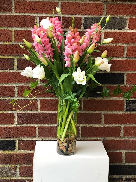 Pink and White elegant Garden - In a tall cylinder clear vase pink snapdragons are woven together with gorgeous pink tulips and white lisianthus.  Flowing over the top of the vase are elegant green ivy.    *We do our best to keep these flowers in stock however  subject to availability substitutions may occur*