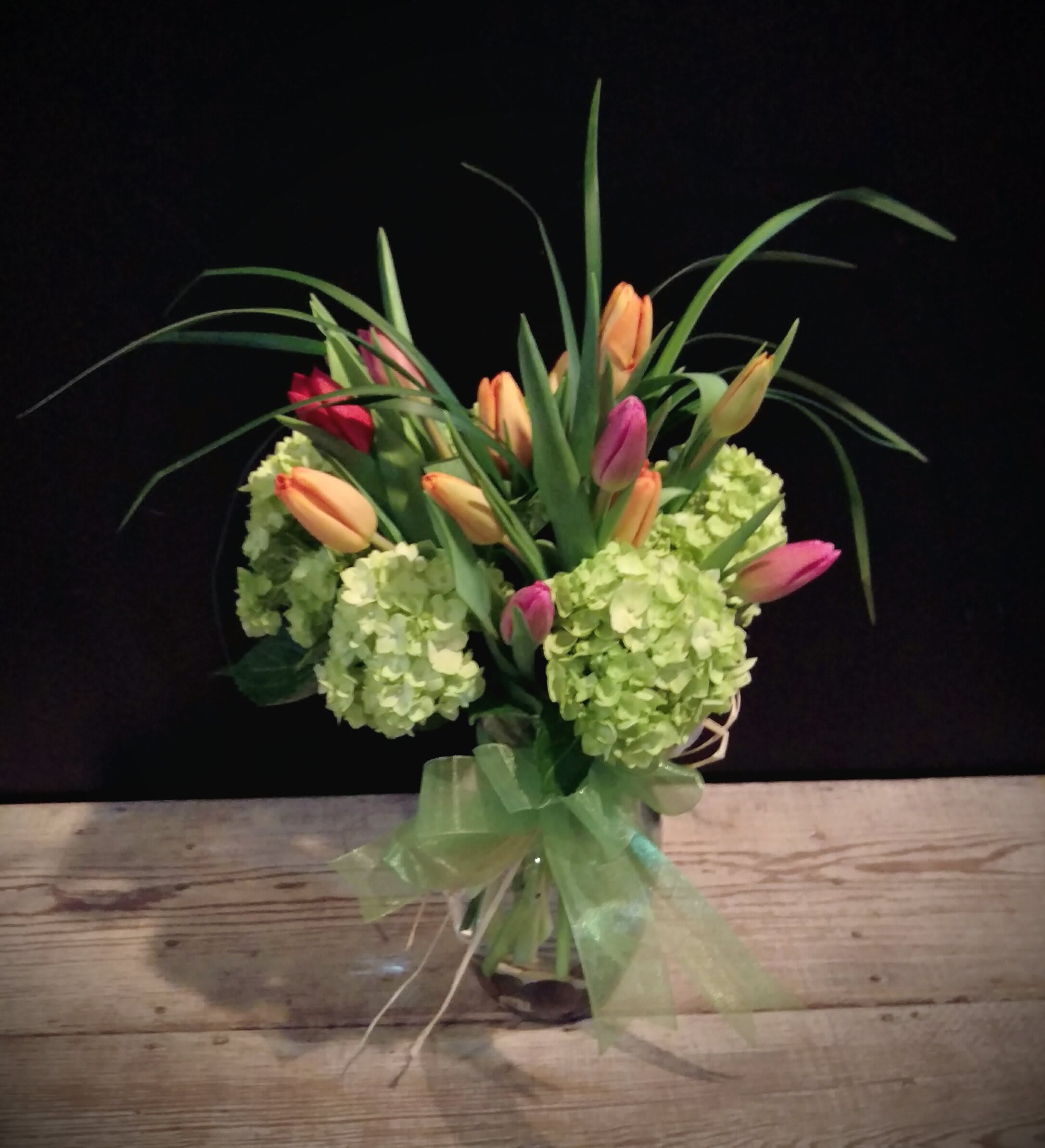 Happy Kiss (tulip colors vary) - This &quot;kiss&quot; features 15 Dutch &quot;tu-lips&quot; in assorted colors springing from bright vibrant green hydrangea.  Gathered with grasses and placed in a vase with riverstones and ribbons...  Perfect way to send your loving wishes for brighter days ahead..   Tulip colors vary weekly  