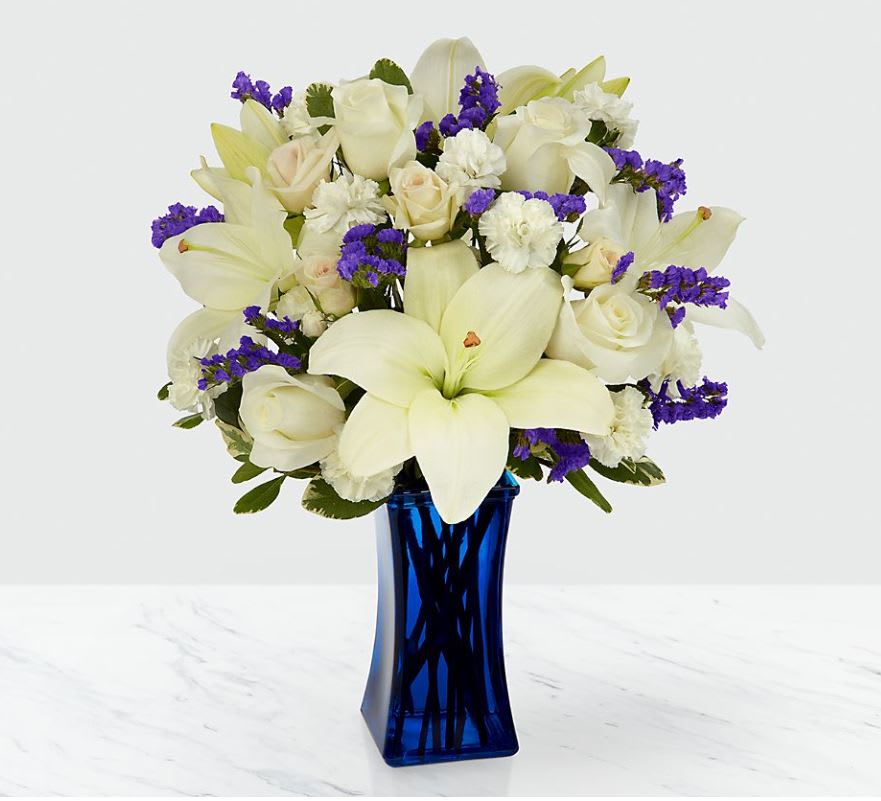 Wishes in Blue - Our  Bouquet features lilies, roses, carnations and lush greens to captivate your recipient. A collection of brilliant white blooms is contrasted by a stunning and bold blue vase. This arrangement makes an excellent thank you, get well or engagement gift! For sharing your sympathies, this bouquet is best fit to send to a home or residence.  