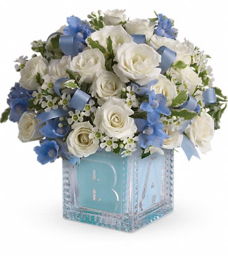 Baby's First Block by Teleflora - Blue Baby's First Block by Teleflora - Blue - Celebrate the coolest baby boy on the block's arrival with this charming glass baby block that arrives chock full of pretty flowers. Perfect for baby showers too! The glass block will make an adorable display piece for years! Dazzling white spray roses light blue delphinium white waxflower and light blue organza ribbon are delivered in a clear baby block with a light blue liner. One great delivery deserves another don't you think?Approximately 10" W x 9 1/2" H Orientation: All-Around As Shown : T34-2ADeluxe : T34-2BPremium : T34-2C