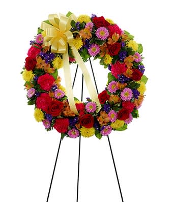 Multi-Color Standing Sympathy Wreath - Sympathy Wreath made up of Red roses, pink carnations, yellow mums, light pink Matsumoto aster, orange alstroemeria and purple statice form this beautiful sympathy wreath which also includes a yellow ribbon and a self-standing easel. Measures 21&quot;H by 21&quot;L
