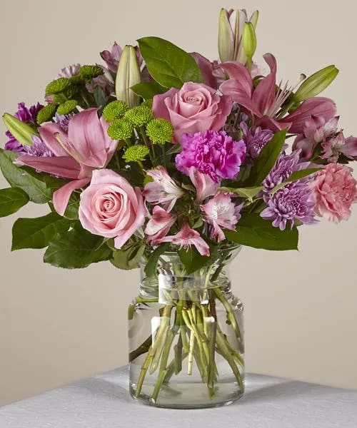 MARIPOSA BOUQUET  - Did you know that when a butterfly crosses your path, it's a sign of good luck? This bouquet offers a mix of ruffled texture, vibrant colors, and positivity to light up any room as soon as it arrives. Pink roses, pink lilies, pink alstromeria, lavender cushion mums, lavender carnations, pink carnations and green mums are gathered together in this modern glass cinched vase creating a gift perfect for any occasion. Standard arrangement measures approximately 15&quot;H x 15&quot;W