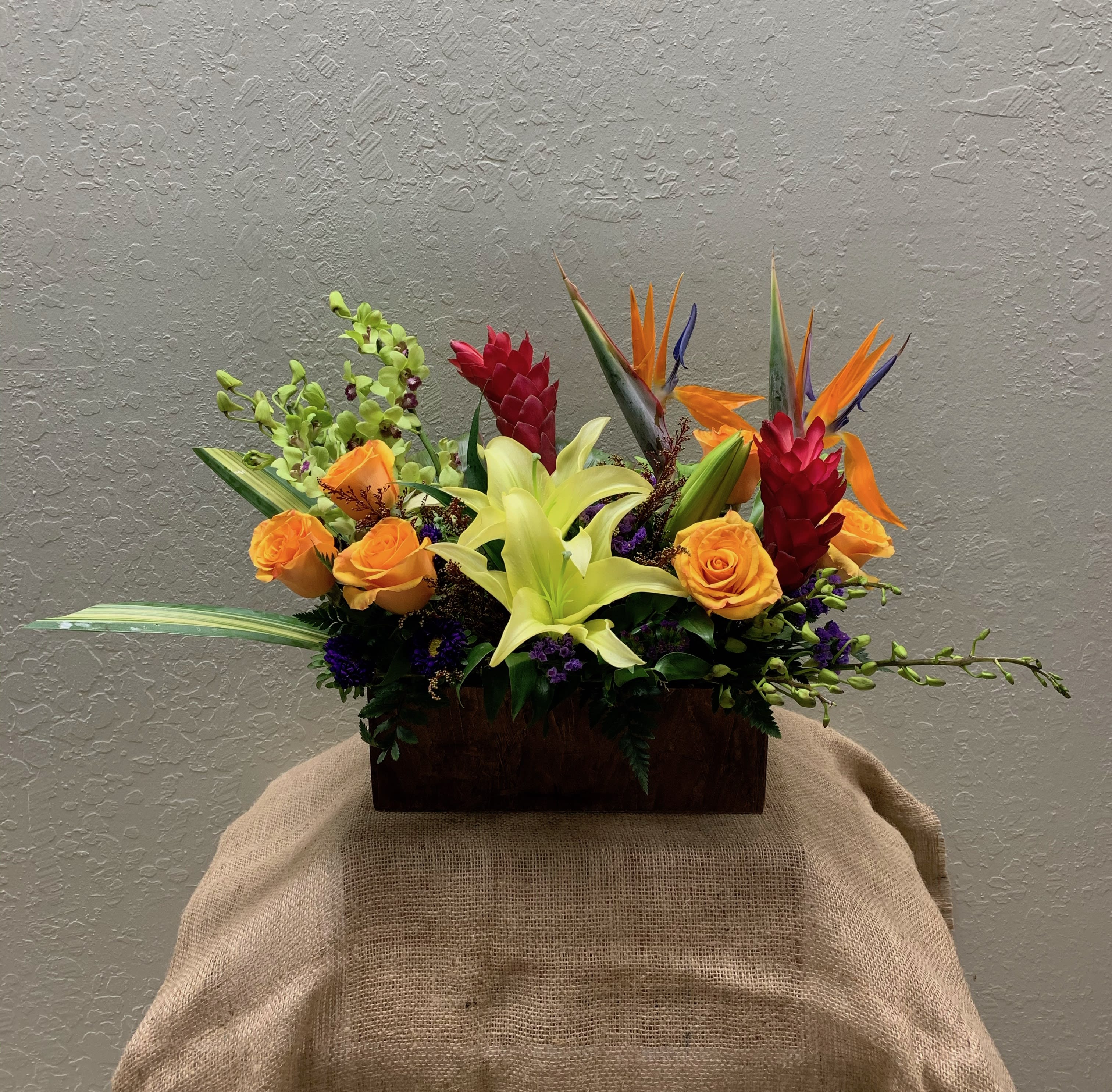 Formosa Island Formosa Island - A colorful tropical arrangement in a wooden planter box featuring, birds of paradise, lilies, dendrobium orchids, roses, filling flowers and filling greens.
