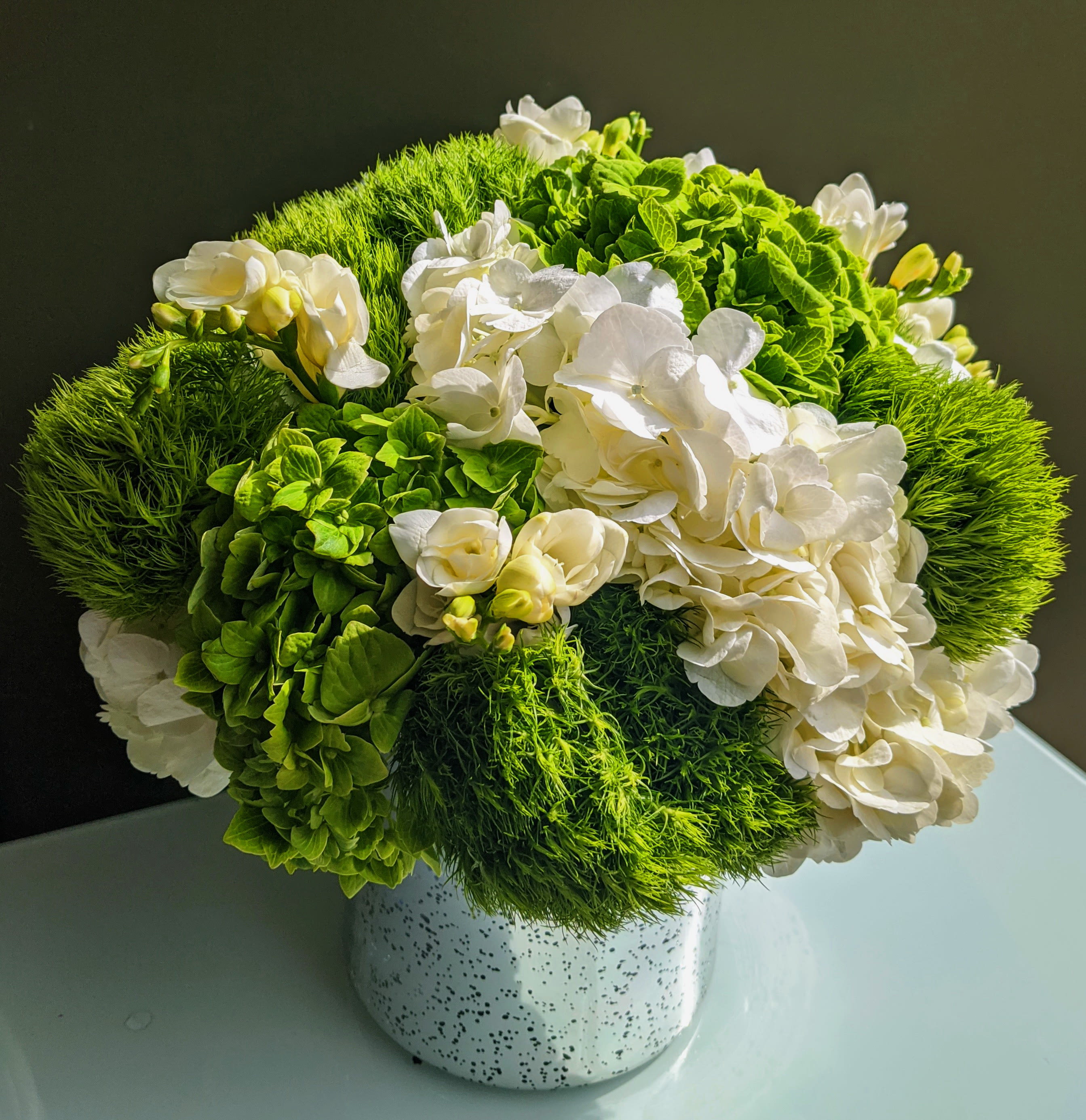 Lush Green and White Hydrangea Pave  - This simple classic arrangement can serve as a gift for any occasion.  simple silver mercury cylinder overflows with lush green and white hydrangea and select seasonal blooms in white and green. 