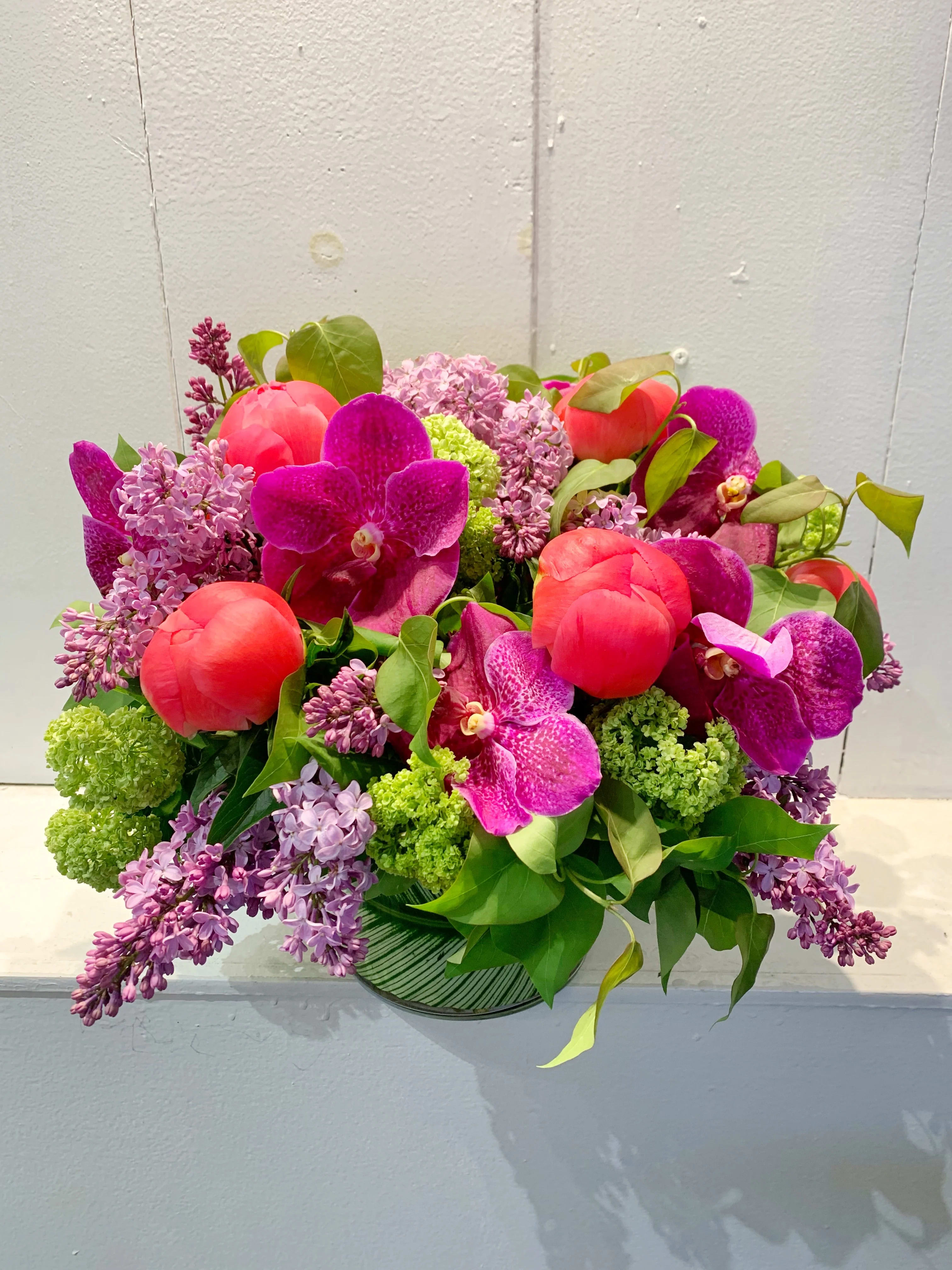 Lilac in the Park - This beautiful arrangement is a combination of beautiful flowers that you will see in the park. Gorgeous purple lilacs, viburnum, peonies and pink orchids. Such elegance in one arrangement. 