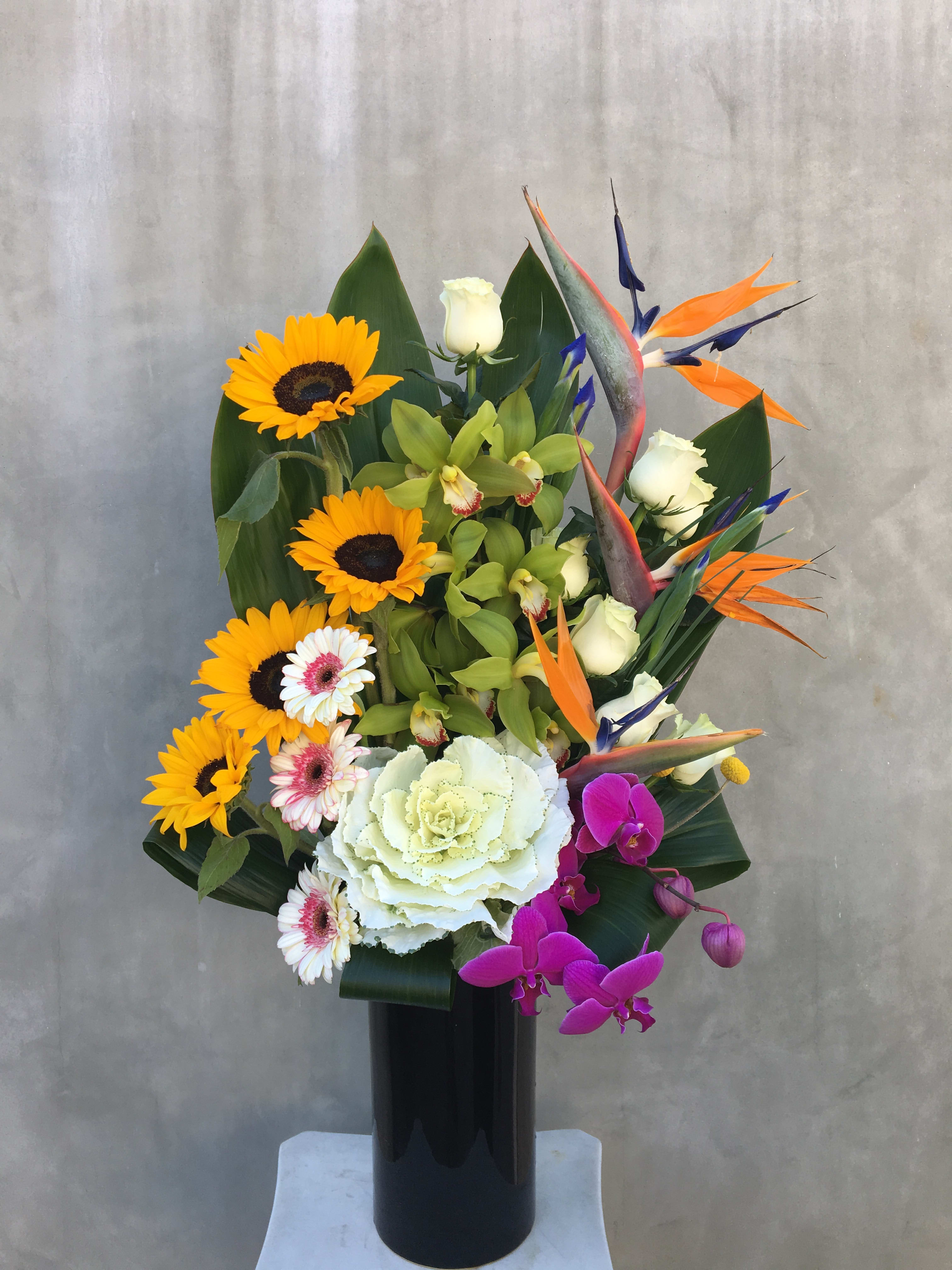High Intense  - EXTRAVIGANTE! Beautiful tropical arrangement, containing orchids, roses, birds of paradise, sunflowers, and much more in a tall vase. 