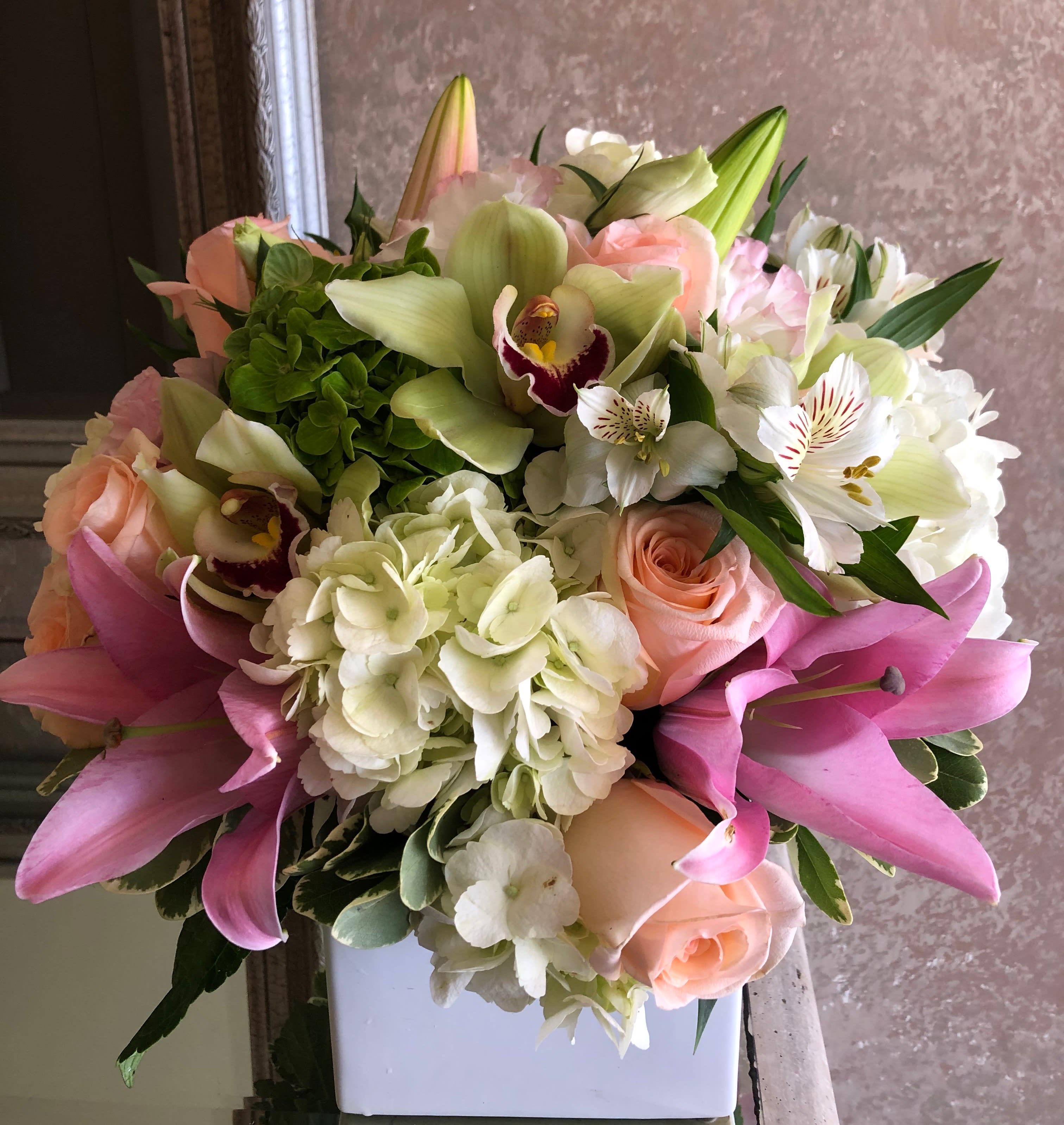 A Mother's Lovey Touch A Mother's Lovey Touch - A stunning, compact flower arrangement made with some of nature's finest blooms, including Hydrangea, Cymbidium Orchids, Roses, and Lilies arranged in a white vase.