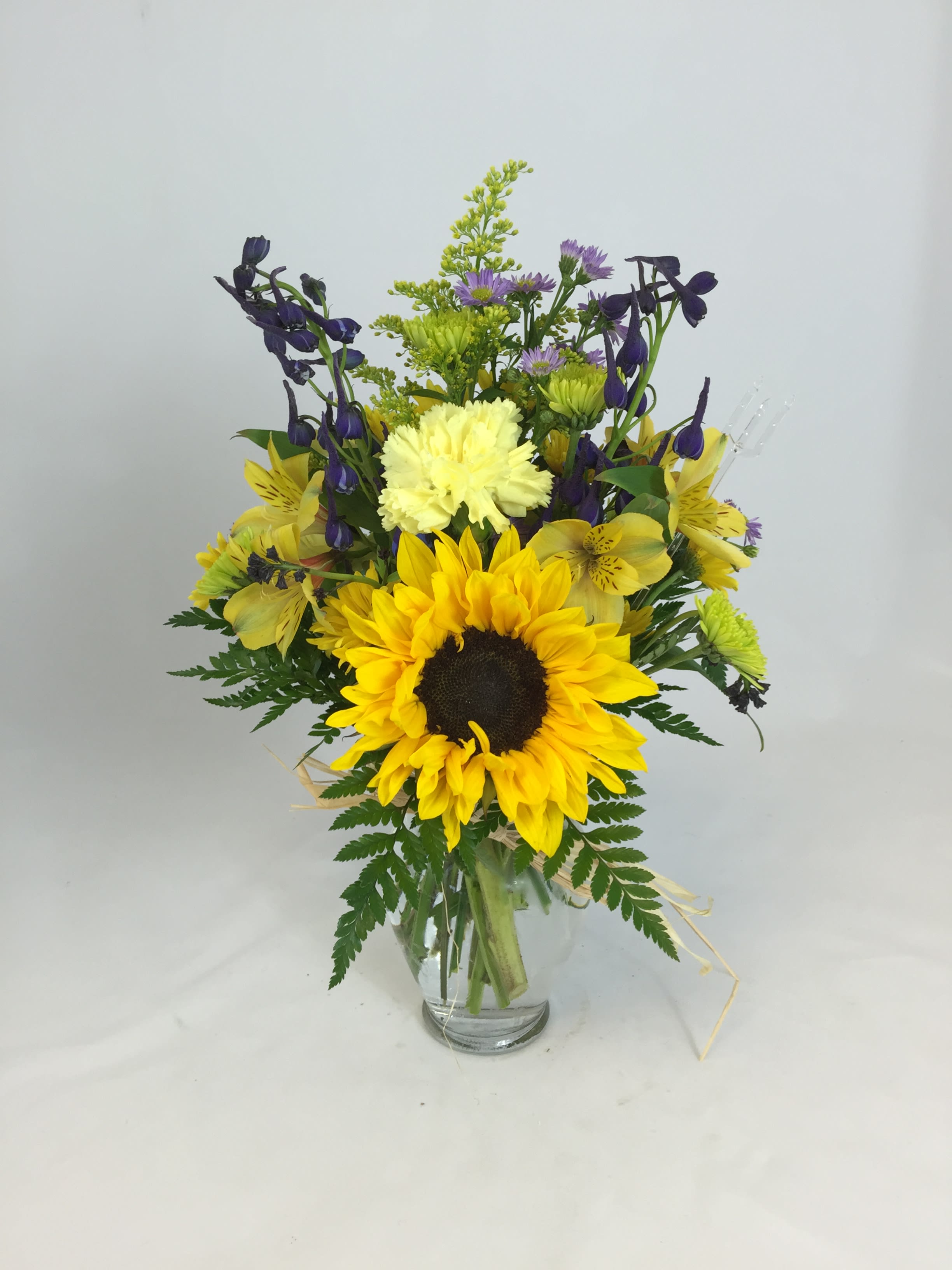 Sunflower Cheer - Sunflowers, Blue Delphinium, Yellow Alstromaria, Yellow Carnations and fillers arranged in a glass vase. 