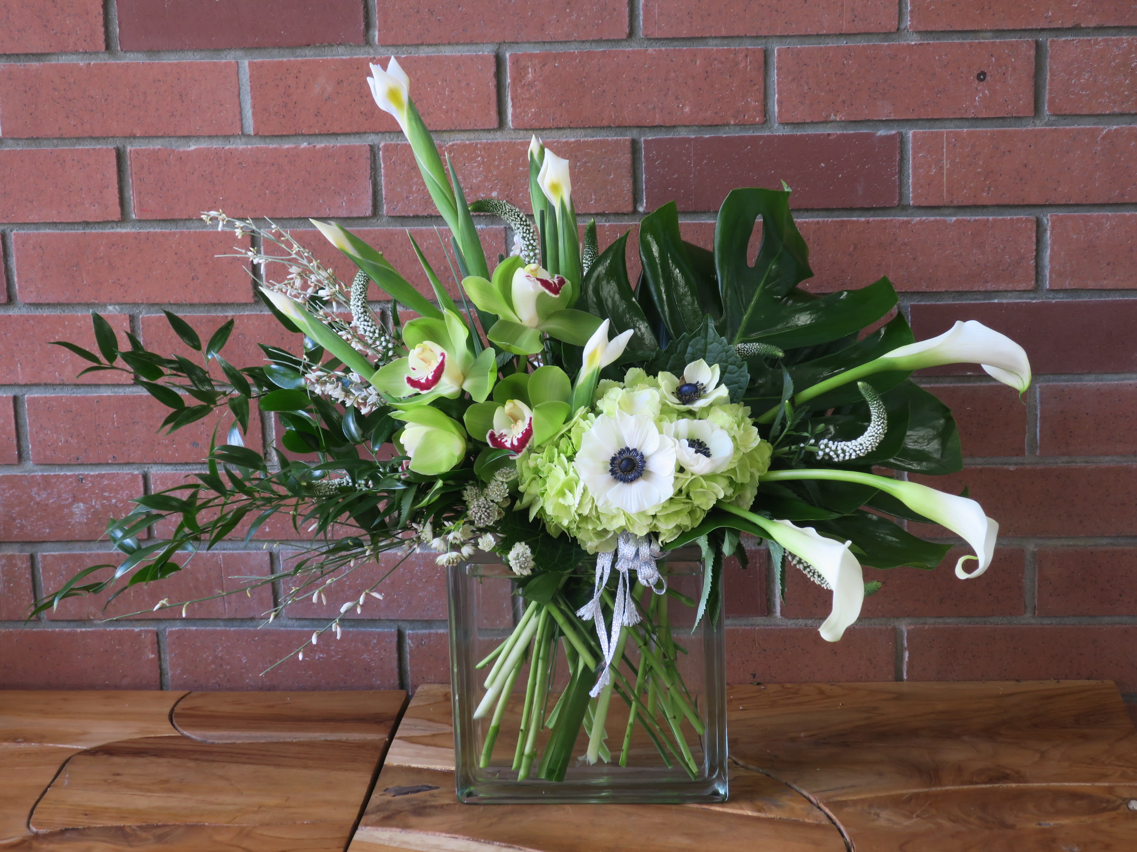 The Crowd Pleaser - Wow your loved ones with this grand arrangement of exotic tropical foliage,hydrangeas, calla lilies, orchids, white iris, anemones, roses and premium fillers in a modern vase 