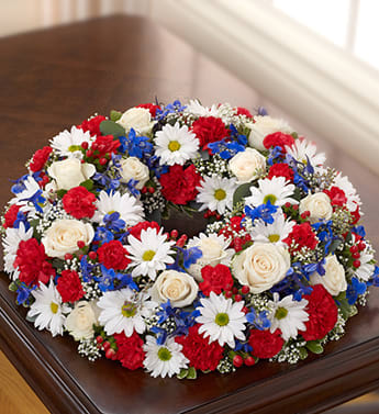 Cremation Wreath - Red, White and Blue - Product ID: 95445   Send a final fitting tribute to a well-loved veteran with our elegant and beautiful red, white and blue table wreath arrangement. Fresh roses, delphinium, carnations, daisy poms and more are hand-crafted and meant to house a treasured photograph or urn at the home or memorial service. Comforting table wreath arrangement of red, white and blue blooms such as roses, delphinium, carnations, hypericum, mini carnations and daisy poms, gathered with gypsophilia, variegated pittosporum and seeded eucalyptus Hand-crafted by our select florists to be sent to the cremation service to honor friends or family members Also appropriate for smaller memorial services in the home The cremation urn or a framed photograph can be placed in the center to present a lovely tribute at the service or home Large arrangement measures approximately 22&quot;H x 22&quot;L Small arrangement measures approximately 17&quot;H x 17&quot;L Our florists hand-design each arrangement, so colors and varieties may vary due to local availability