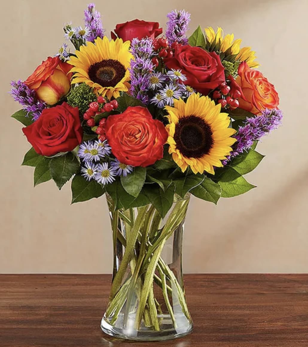 Country Medley - All-around arrangement with red roses and hypericum, autumn-colored roses, sunflowers, purple liatris and monte casino; accented with assorted greenery Deluxe size shown
