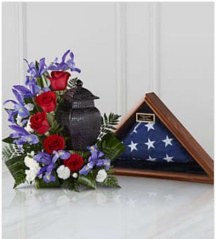  Patriotic Tribute™ Arrangement - Honor a loved one's devotion to their country with a floral tribute proudly blooming in a flag-inspired red, white and blue. So appropriate for celebrating the life of a veteran, government worker or any American patriot, this graceful crescent of flowers includes red roses, white carnations and blue irises complemented by lush greens. It makes a touching setting for an urn or for displaying meaningful mementos such as service photographs or folded honor guard flags. Fitting for display at wakes, funeral or memorial services or at home during condolence calls. Measures approximately 18&quot;H x 17&quot;W. Please note that the flag and case (pictured) are not included with this item. Your purchase includes a complimentary personalized gift message.
