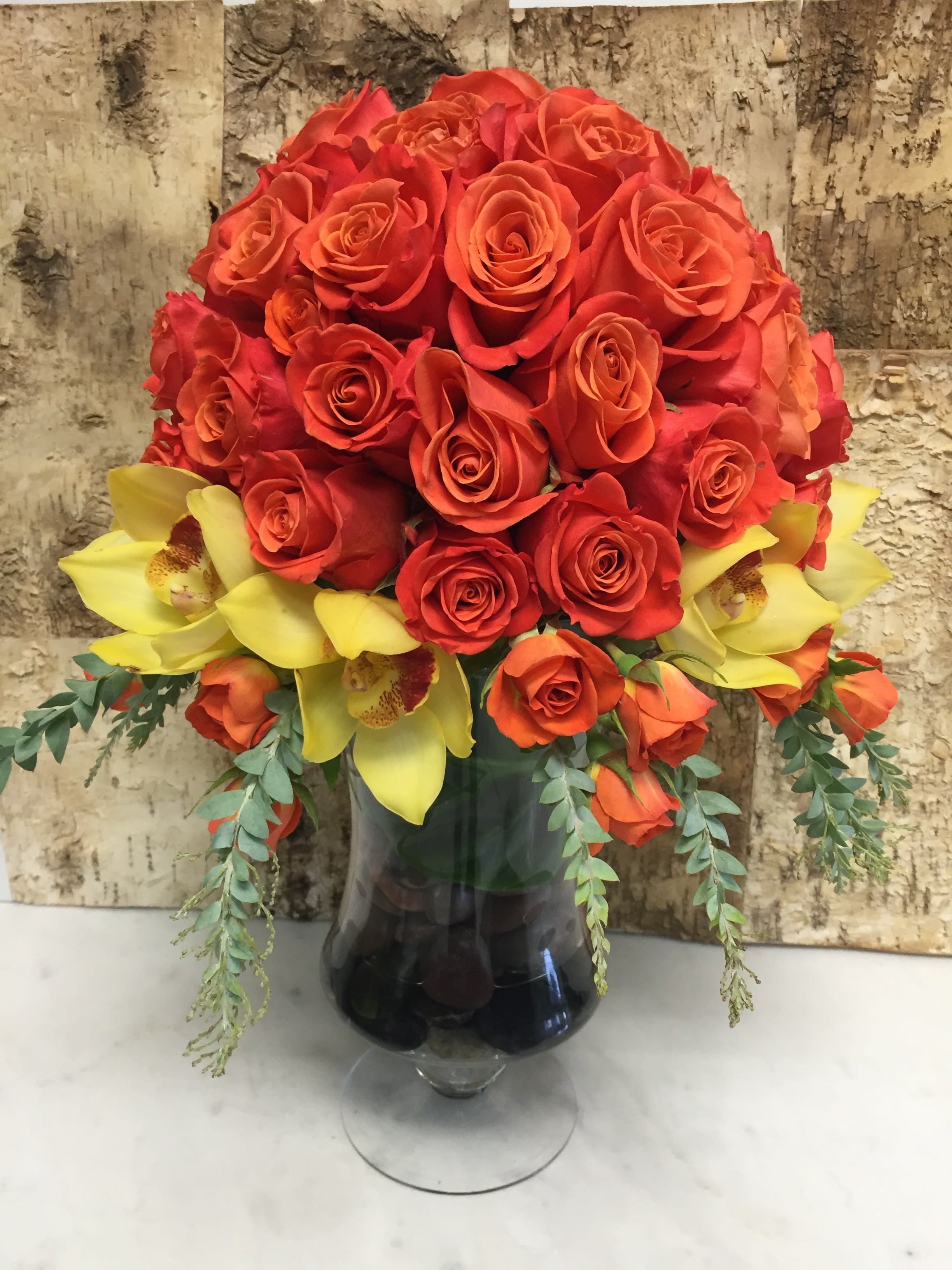 Citrus Delicacies Citrus Delicacies - This beautiful hand made arrangement contains orange roses with yellow cymbidiums and sprayed roses sitting in a vase with river rocks to remind you of the Miami warmth and sunset.