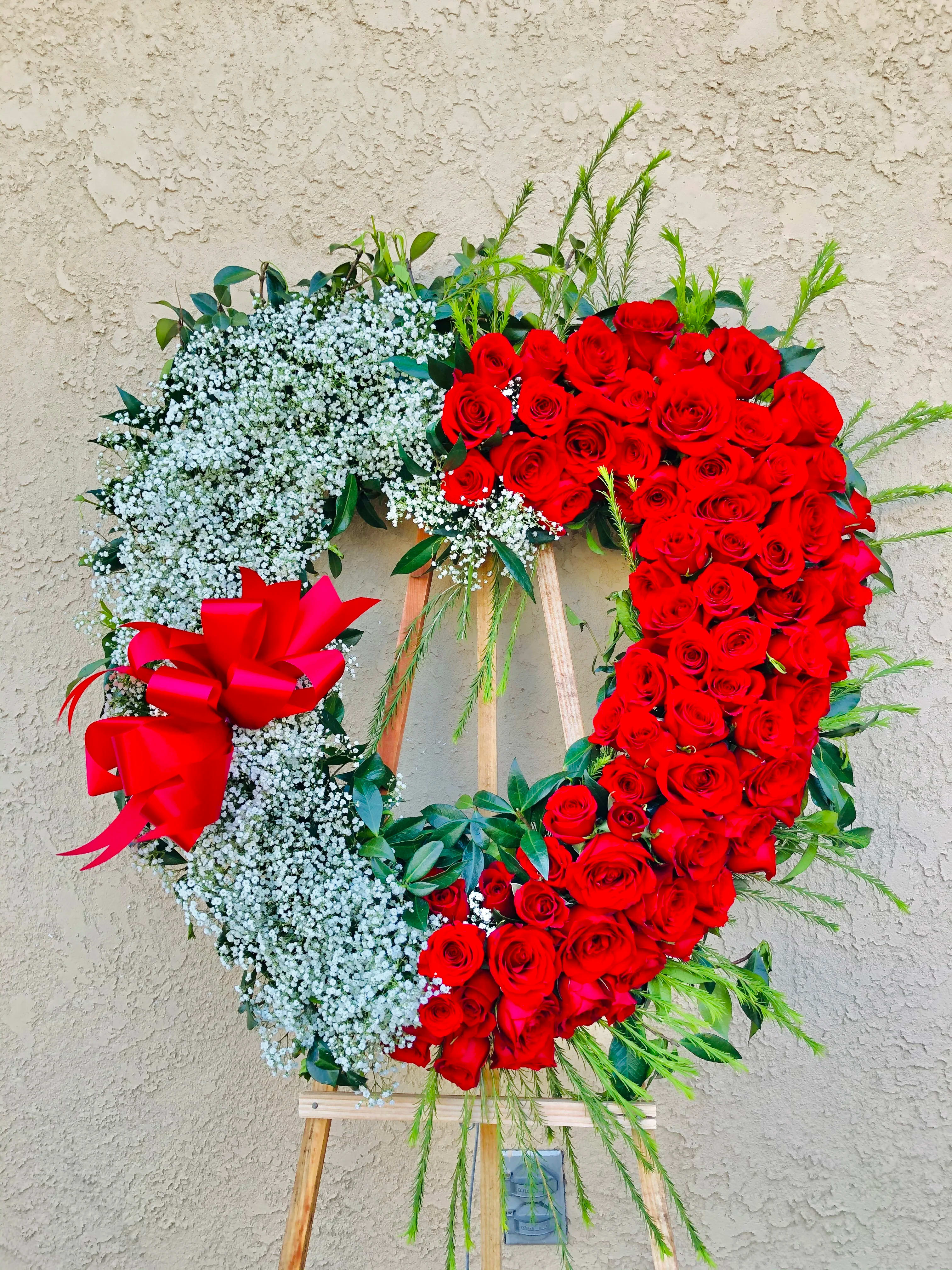 Encompassing Love Funeral Spray - A mixture of premium red roses and baby breathes in a heart-shaped standing spray with green accents. 