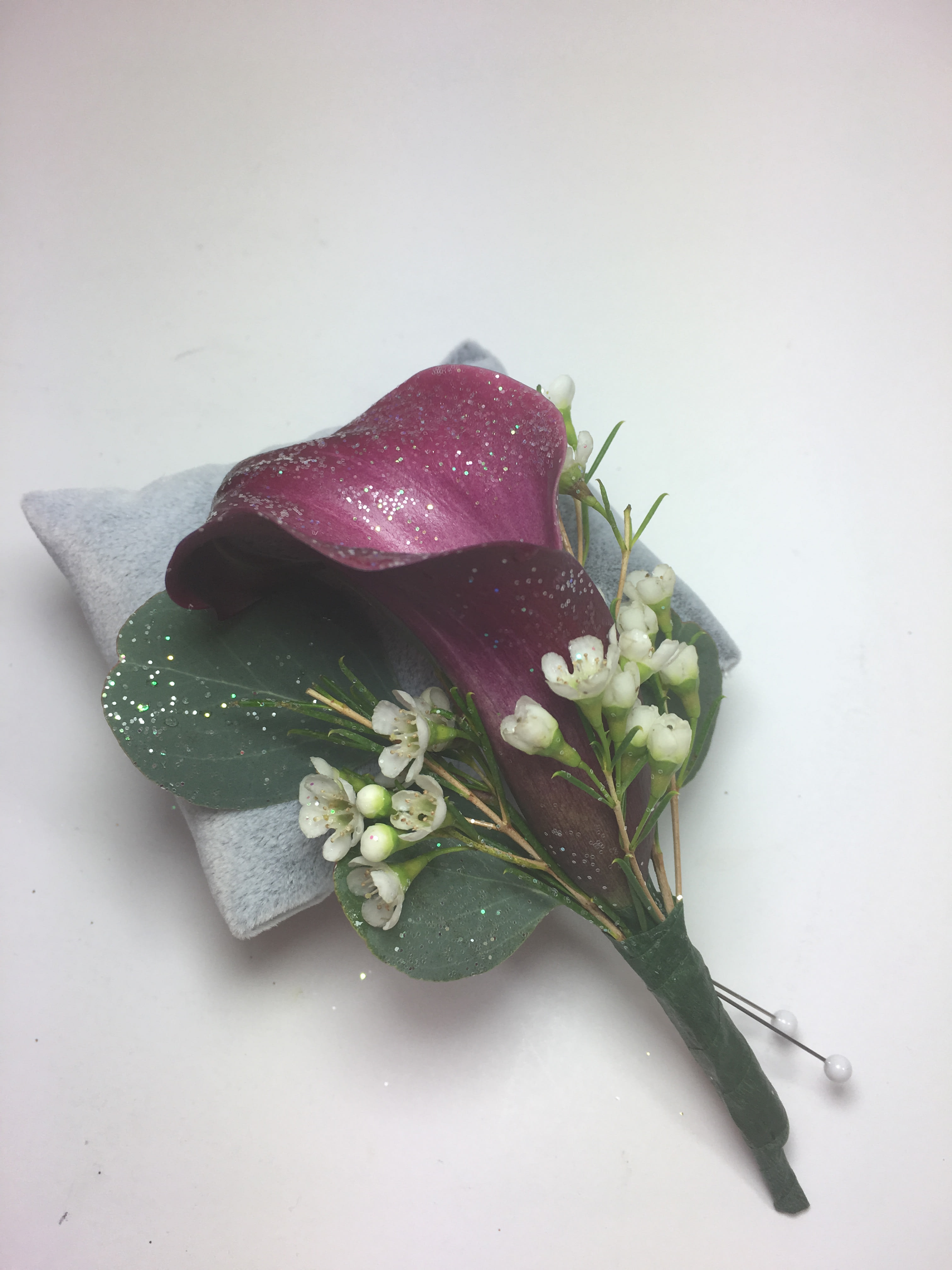 B6 Burgundy Calla lily Boutonniere B6 Burgundy Calla lily Boutonniere - To complement her clutch, elegant lily for the gentleman. Prom orders are customized to your date and her amazing dress.