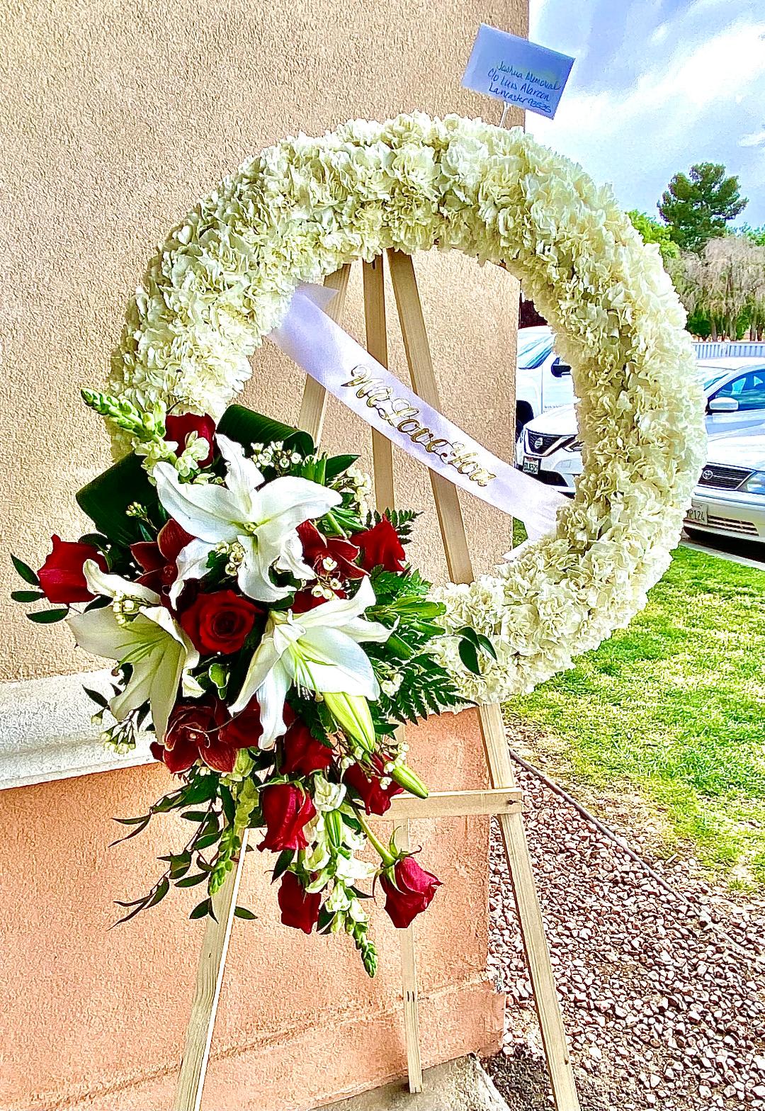 Dedicated with Love Dedicated with Love - This delicate wreath is composed of White Carnations and accented with White Lilies, Red Roses, Burgandy Cymbidium orchids, White Snapdragon, and various foliage. This design measures approx. 24" in diameter.