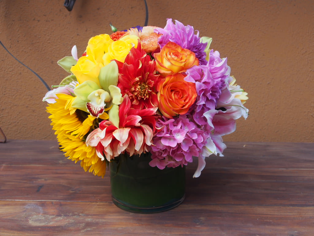 Cheerful Cheerful - Colerful mix of seasonal flowers like dahlias, roses, hydrangeas and sunflowers in 6" clear vase cylinder.