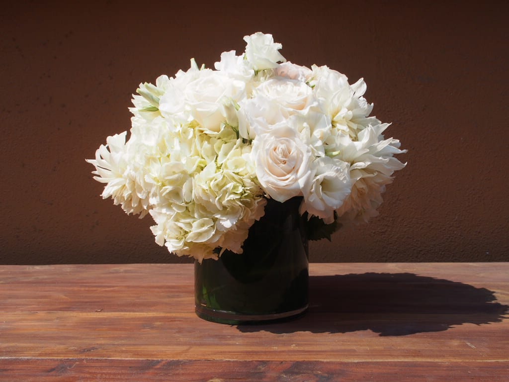 Snow White Snow White - 5" clear vase cylinder with green leaf inside holding white and off white flowers like roses, lisianthus, dahlias and hydrengeas.