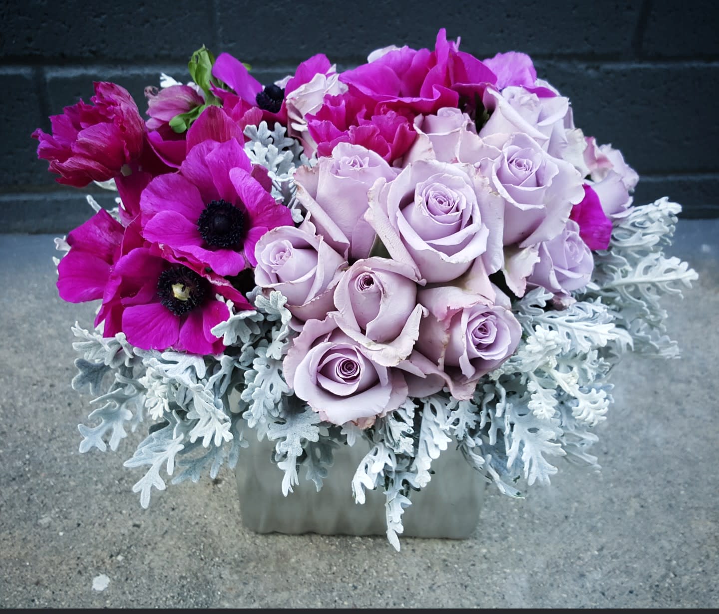 PASTEL PETALS - This Pastel Lavender roses with Anemone if available  is in a short small silver vase. Great for any type of occasion! (Florals and container might vary due to availability.) Note: If you would like to change floral color, please add your request in the note section when placing your order.