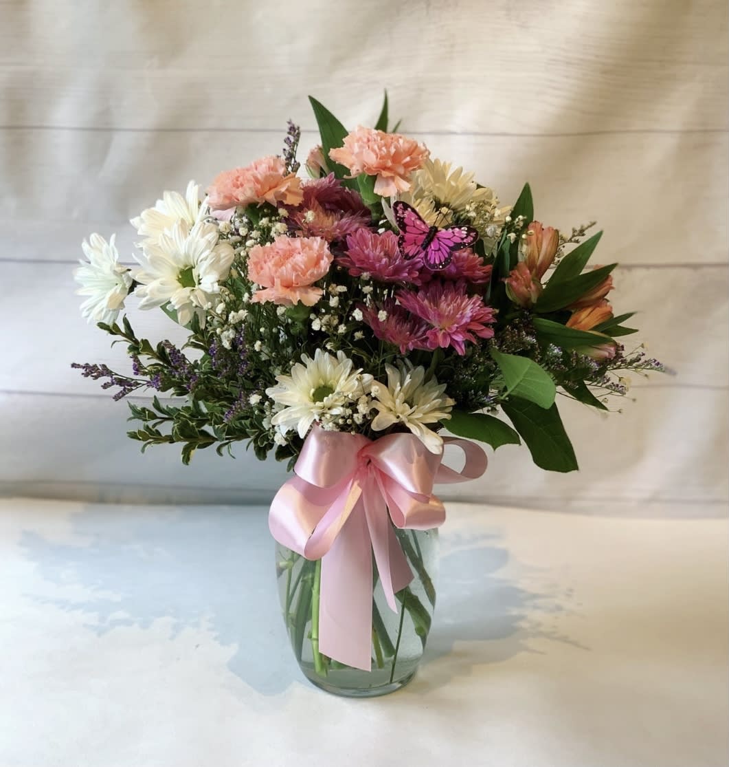 Beautiful Butterflies  - This beautiful arrangement of soft pinks, whites and lavenders is perfect for a variety of occasions. Featuring multiple colored daisies, carnations, babies breath and alstroemerias, it's a gorgeous display of friendship, love, congratulations and cheer. It's complimented with a pretty butterfly friend and a soft, handmade, bow. 