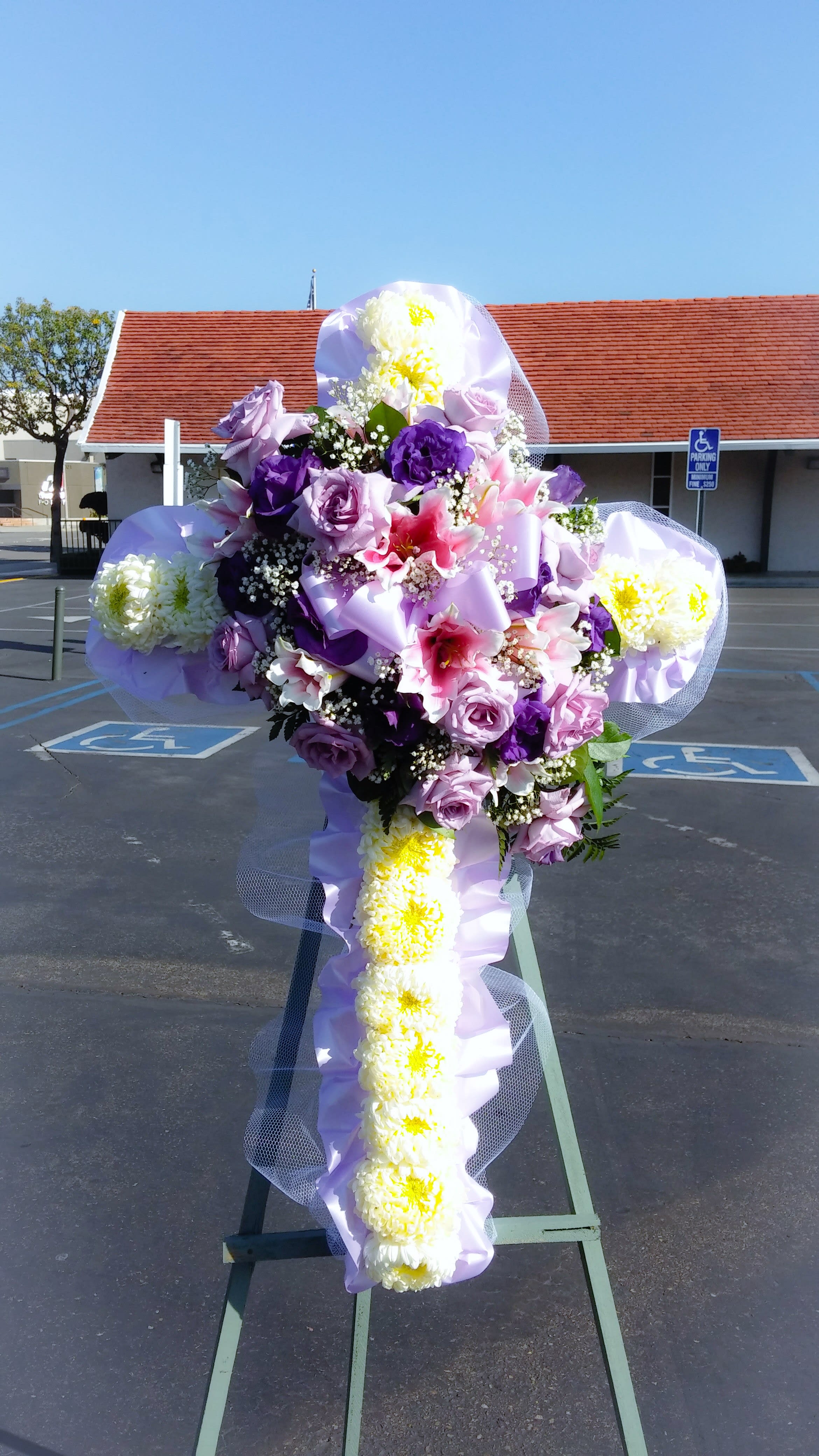 Sympathy Cross - Floral cross made with chrysanthemums and decorated with a spray of roses and lilies.   Sympathy arrangements require more prep time, please place your order at least 5 hours prior to start of viewing or service.  For optimal quality, we recommend placing your order with a minimum of one day's notice.