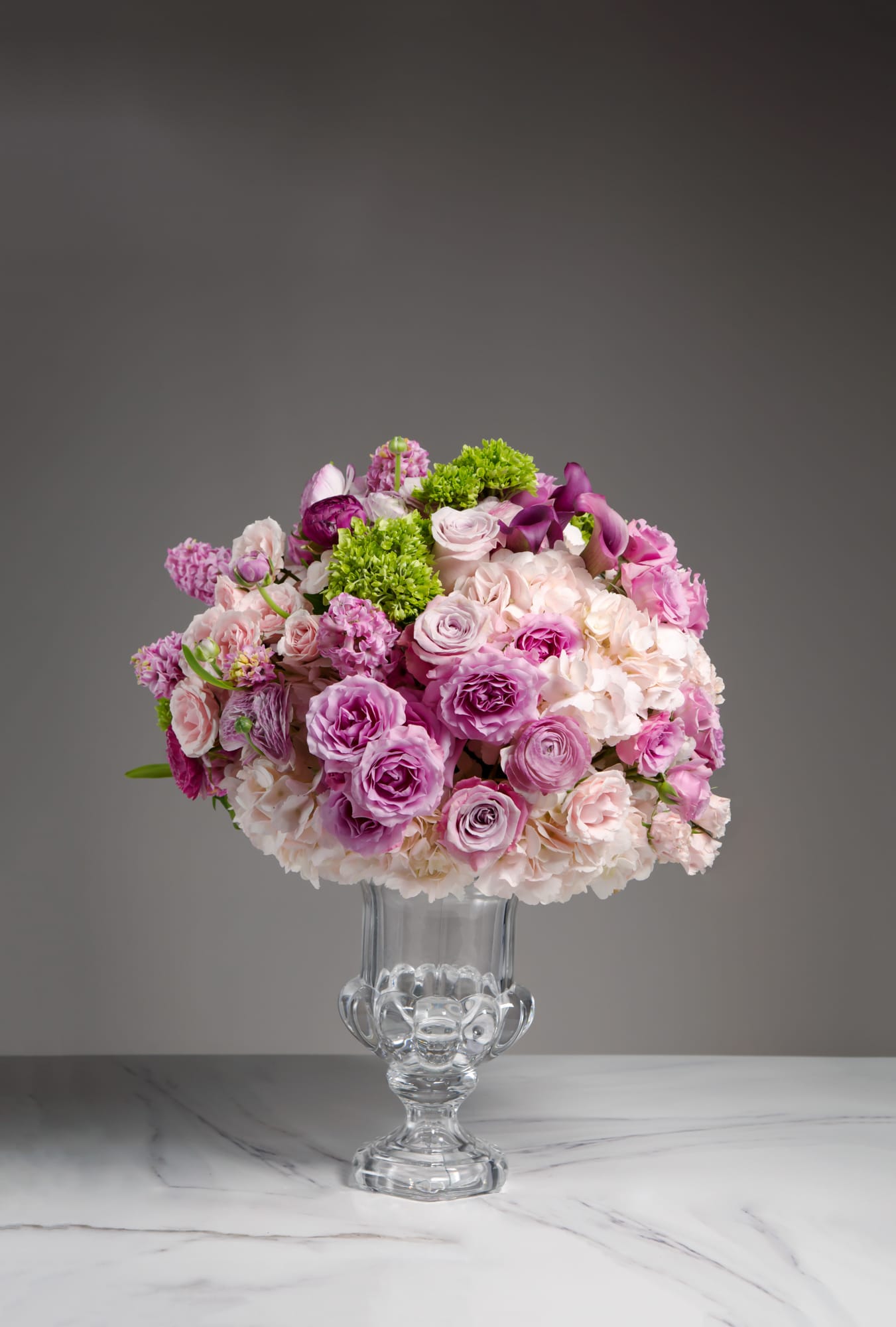 Lavender Grande  - Rising from the clear tall vase like a tide of relaxation, the Lavender Grande is shaded in both warm pink and splashes of royal purple with green hydrangea accents. Perfect for your foyer or entryway piece! 