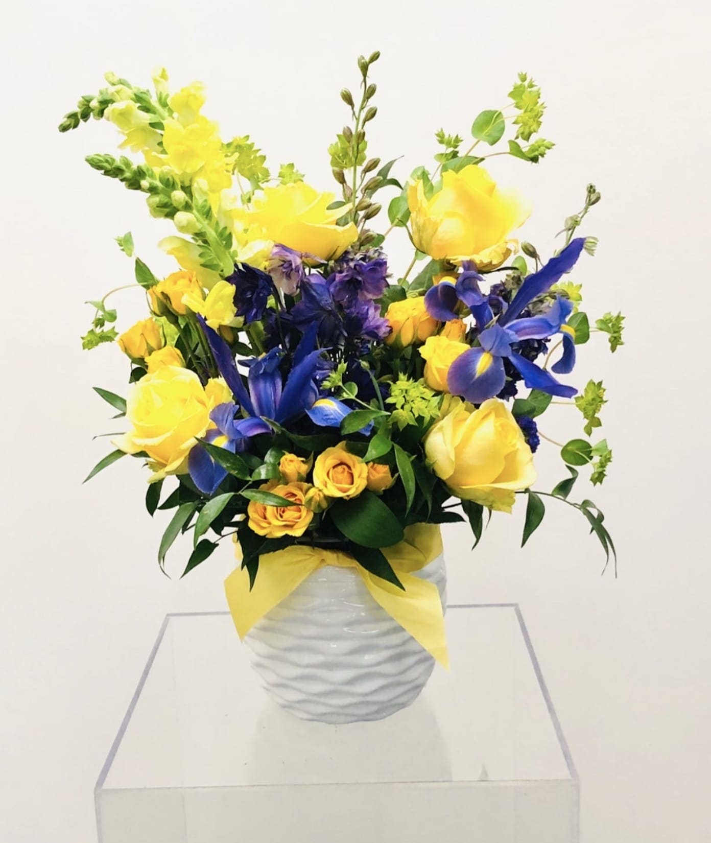 Ribbon in the Sky - Bright and delightful floral design that looks like rays of yellow sunshine are flowing from it.  The flowers used in the design are roses, iris, delphinium, snapdragon, spray roses and greenery.  Floral arrangement to be placed in a neutral vase.  *Please view policy section regarding substitutions.