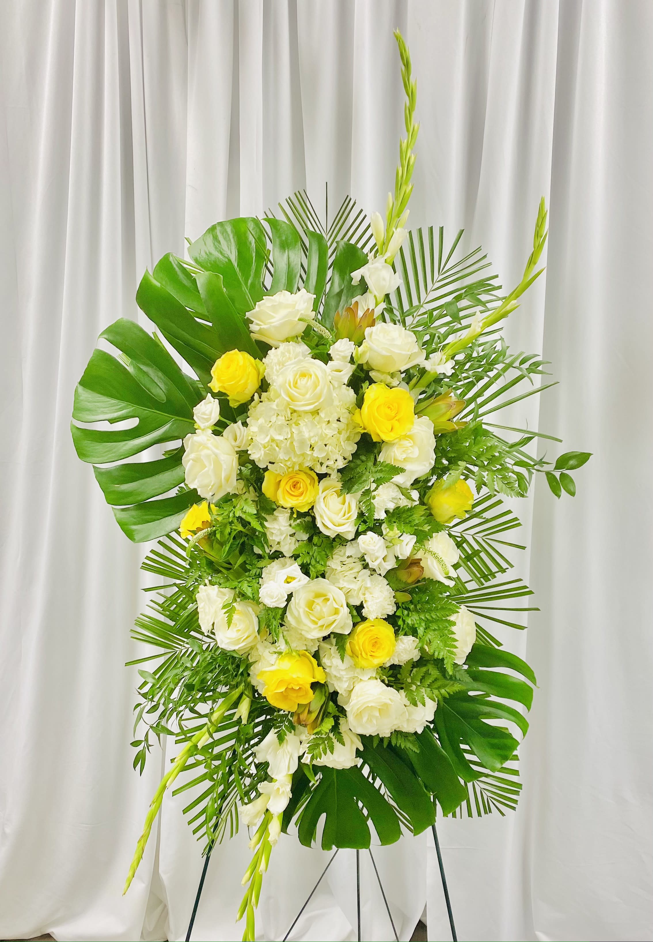 Love and Devotion - Pay your respects to a loved one with this grand standing spray of monstera leaves accented with the classic beauty of yellow and white roses, and celebrate a life of accomplishment and devotion.
