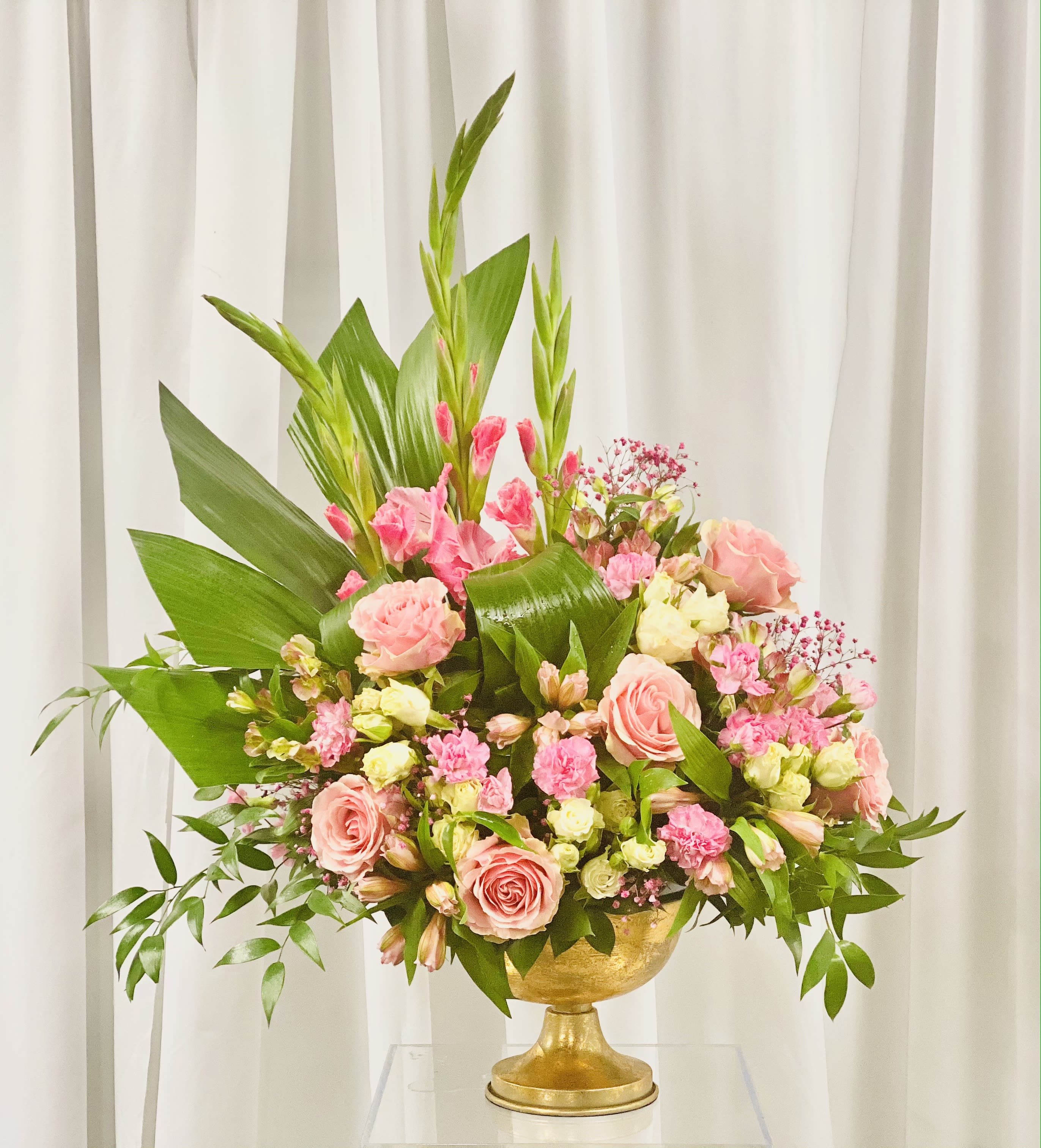 Pink Panther - Strong design lines of greenery and gladiola make a strong statement. The added full display of roses, spray roses, alstroemeria, and mums make for a beautiful floral arrangement.  Flowers set in a neutral vase.