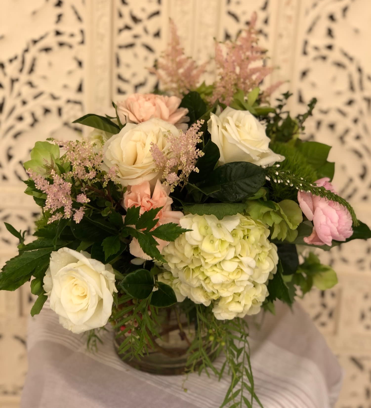 Emma - Gorgeous collection of whites, greens, blushes and pink accents all presented in a clear glass cylinder vase and arranged with a multitude of textures and seasonal foliage to highlight their beauty.  May include hydrangea, roses, peony, helleborus, dianthus, veronica or other seasonal and fresh offerings of the day.