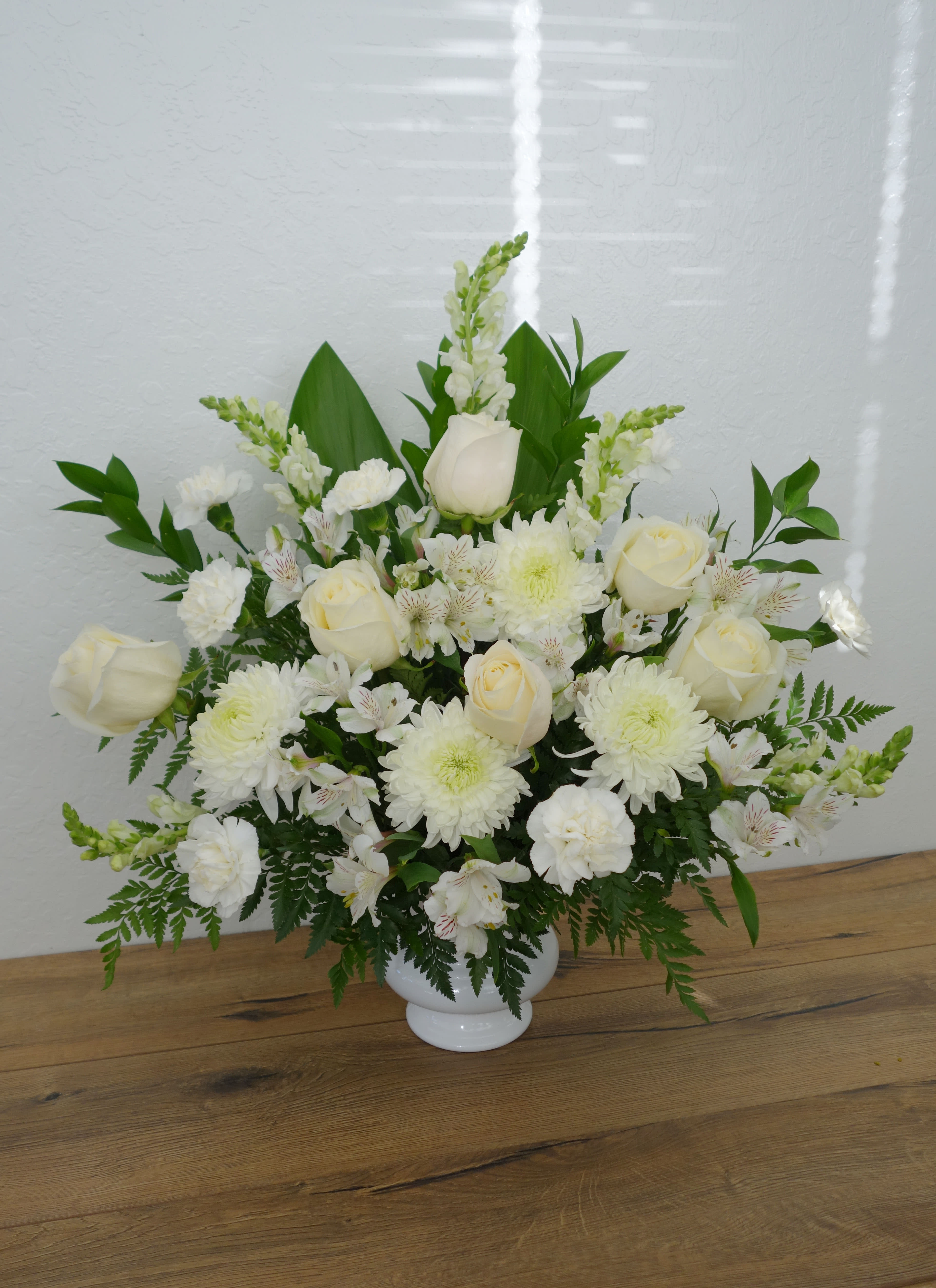 FB#03 Happiness in Heaven Basket - Your love will be warmly felt by the family with this lovely gift of white roses and other favorites in a silver jardiniere vase. Tasteful and elegant, it is a beautiful choice. The exquisite bouquet includes white roses, white alstroemeria, white carnations, white snapdragons and white spider chrysanthemums, accented with assorted greenery.  Orientation: One-Sided  The arrangement is approximately 24&quot; H and 24&quot; W.