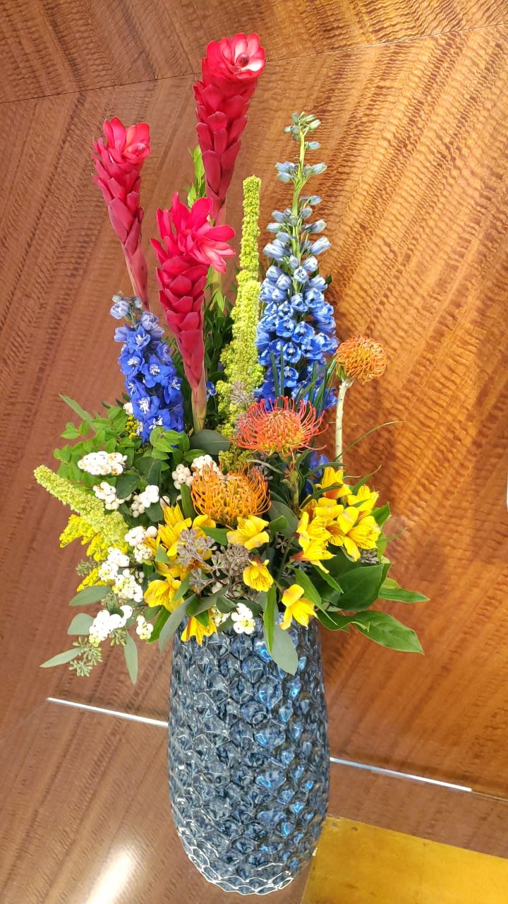 Tropic Like It's Hot Tropic Like It's Hot - An over-sized composition designed to WOW! Includes tropical ginger,bold blue hybrid delphinium, pin cushion protea and alstromeria in a modern tall vase. Seasonal substitution may apply.