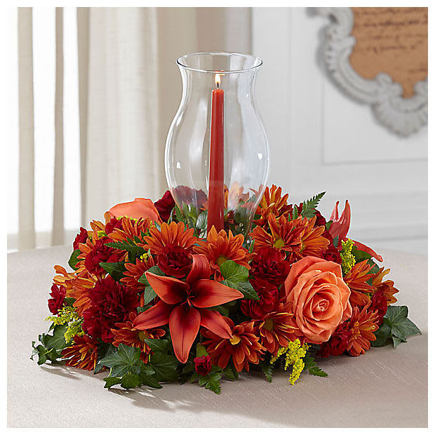Heart of Harvest Centerpiece Heart of Harvest Centerpiece - A beautiful centerpiece for any table. Bronze daisy's, burgundy mini carnations, regular carnations, orange roses, solidago and red lily's. A candle and a hurricane glass cover are included (Due to availability we may have to sub the color of the candle and style of the hurricane glass, but we will sub as similar as possible.)