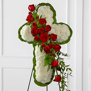 The FTD® Floral Cross Easel - The FTD® Floral Cross Easel is a symbol of love and faith to honor the deceased at the final farewell service. White carnations are arranged to form a cross in which an accent of red roses, spray roses, and lush greens are draped across the center, creating a beautiful display of serene elegance. Displayed on a wire easel.