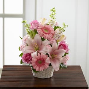 The FTD® Whispering Love™ Arrangement  - This fresh, pink bouquet makes a perfect tribute to honor a special someone who, friends, colleagues and family remember as “simply sweet.” This understated tribute handcrafted by an FTD artisan florist is a lovely pink arrangement of roses, larkspur, carnations, gerbera daisies and Asiatic lilies beautifully accented with vibrant greens in a white basket. It brings a touch of color and beauty for a wake, funeral service or to console family or friends at home.