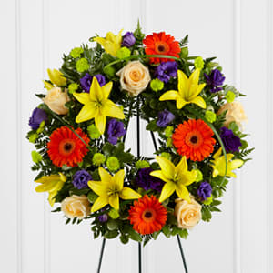 The FTD® Radiant Remembrance™ Wreath - The FTD® Radiant Remembrance™ Wreath is a brilliant burst of color and light that honors a life full of joy and beauty. Crème de la Crème roses create a symbol of peace arranged amongst the vibrant hues of purple lisianthus, orange gerbera daisies, orange Asiatic lilies, green button poms, and a variety of lush greens, forming wonderful representation of a life well lived. Displayed on a wire easel.