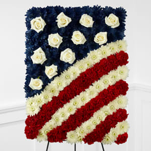 The FTD® Glory Be™ Flag Tribute - The FTD® Glory Be™ Flag Tribute is a symbol of patriotic beauty to commemorate the life of your loved one at their final farewell service. Red carnations, white chrysanthemums and blue dyed white chrysanthemums create a stirring arrangement in the likeness of the American flag with white rose accents to symbolize the stars. Displayed on a wire easel, this exquisite arrangement will bring comfort and peace to their family and friends.
