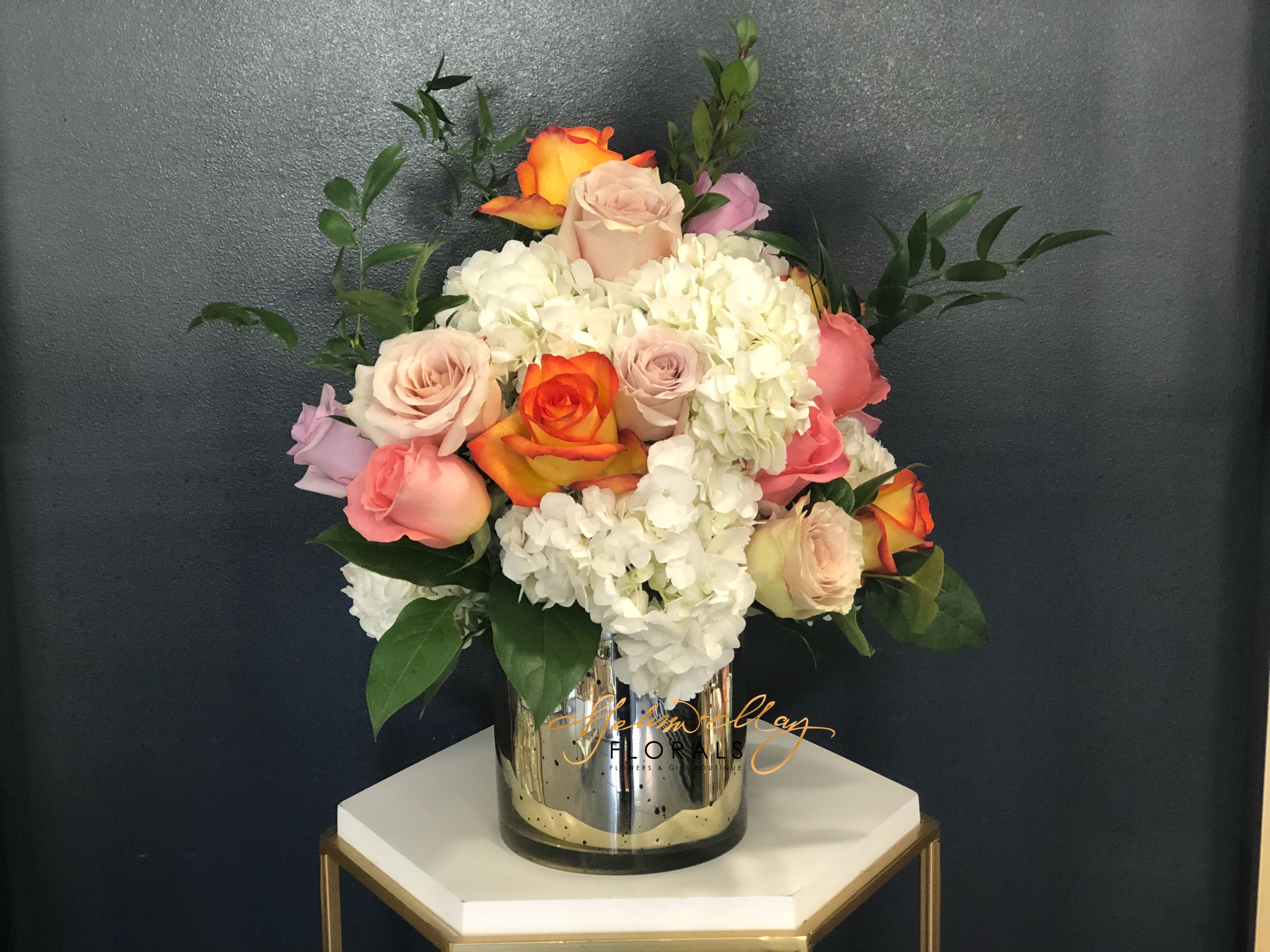 Enchanted Gardens - An all-around arrangement with an assortment of roses and hydrangeas with assorted greenery Artistically designed in a clear glass cylinder vase. Specified which option you prefer to pick from 1 or 2 in special notes. (Deluxe Shown)