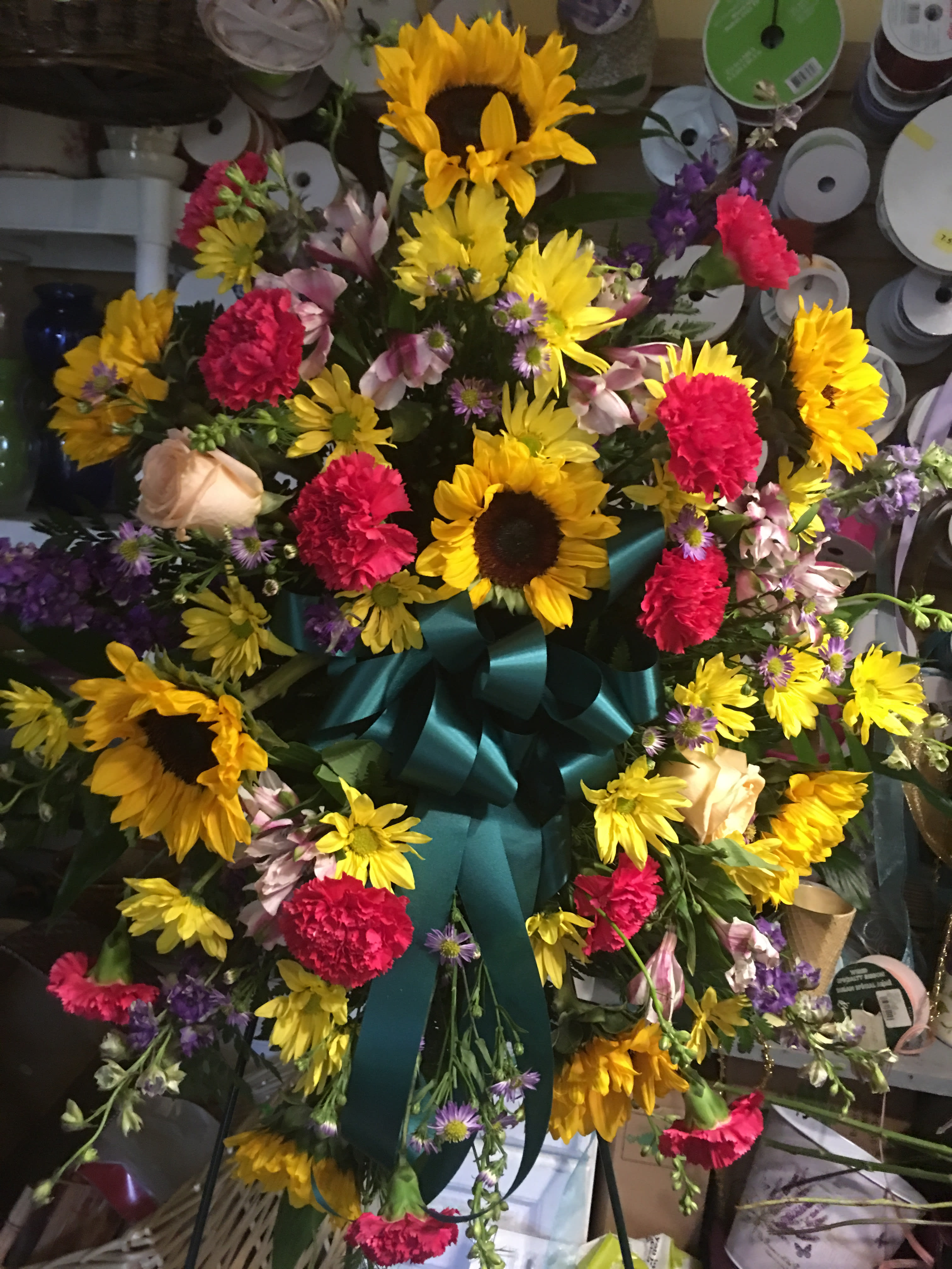 Gardens Tribute Spray Gardens Tribute Spray - Your sincere wishes for peace and harmony resonate beautifully in this perfectly balanced arrangement of bright sunflowers and hot pink carnations balanced with light peach roses adorn this standing spray * colors may vary to ensure the freshest blooms