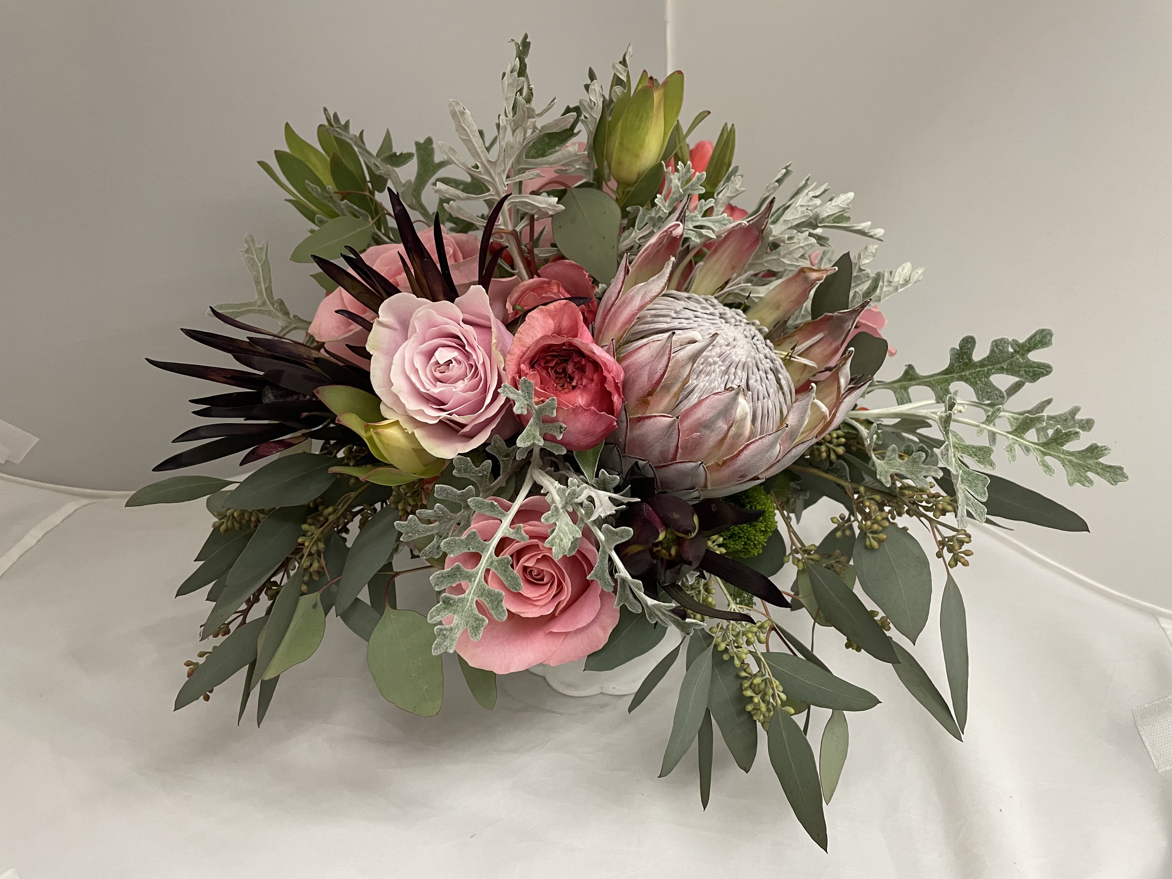 Pretty in Pink - Elegant arrangement with pink garden roses, protea and fresh greens. Occasionally, substitutions of flowers are made based on seasonality and market availability though the overall color and theme of the arrangement will be the same.    