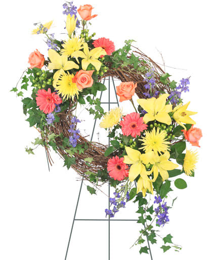CELEBRATION OF LIFE STANDING SPRAY CELEBRATION OF LIFE STANDING SPRAY - Stunning yellow lilies and vibrant orange Gerberas are the perfect tribute for a loved one who was close with nature. The woodsy theme of our Celebration of Life standing wreath is ideal for any funeral service, memorial service, or wake.